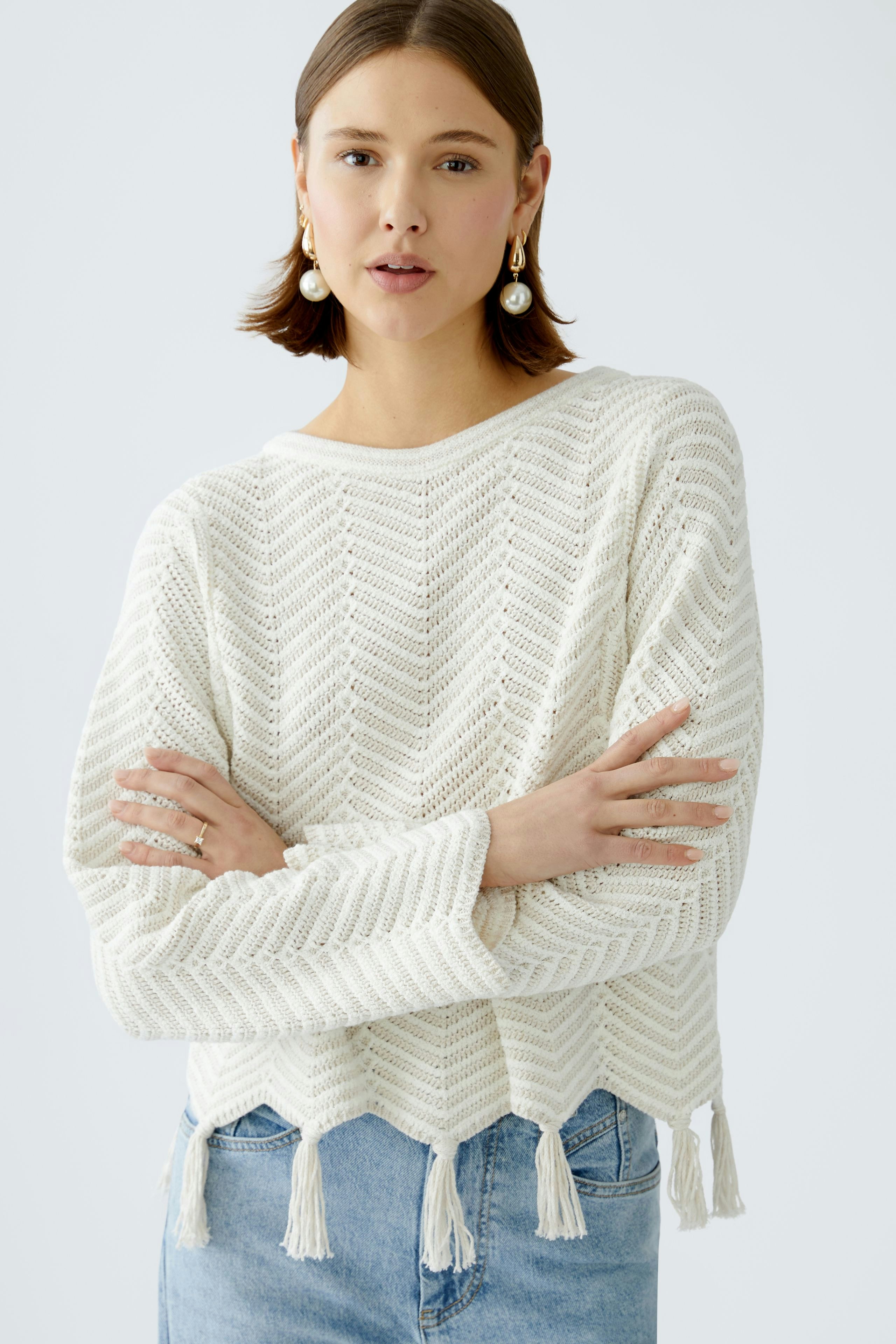 Damen-Pullover: Junge Frau in einem weißen, gestrickten Pullover mit Fransen und Chevron-Muster.