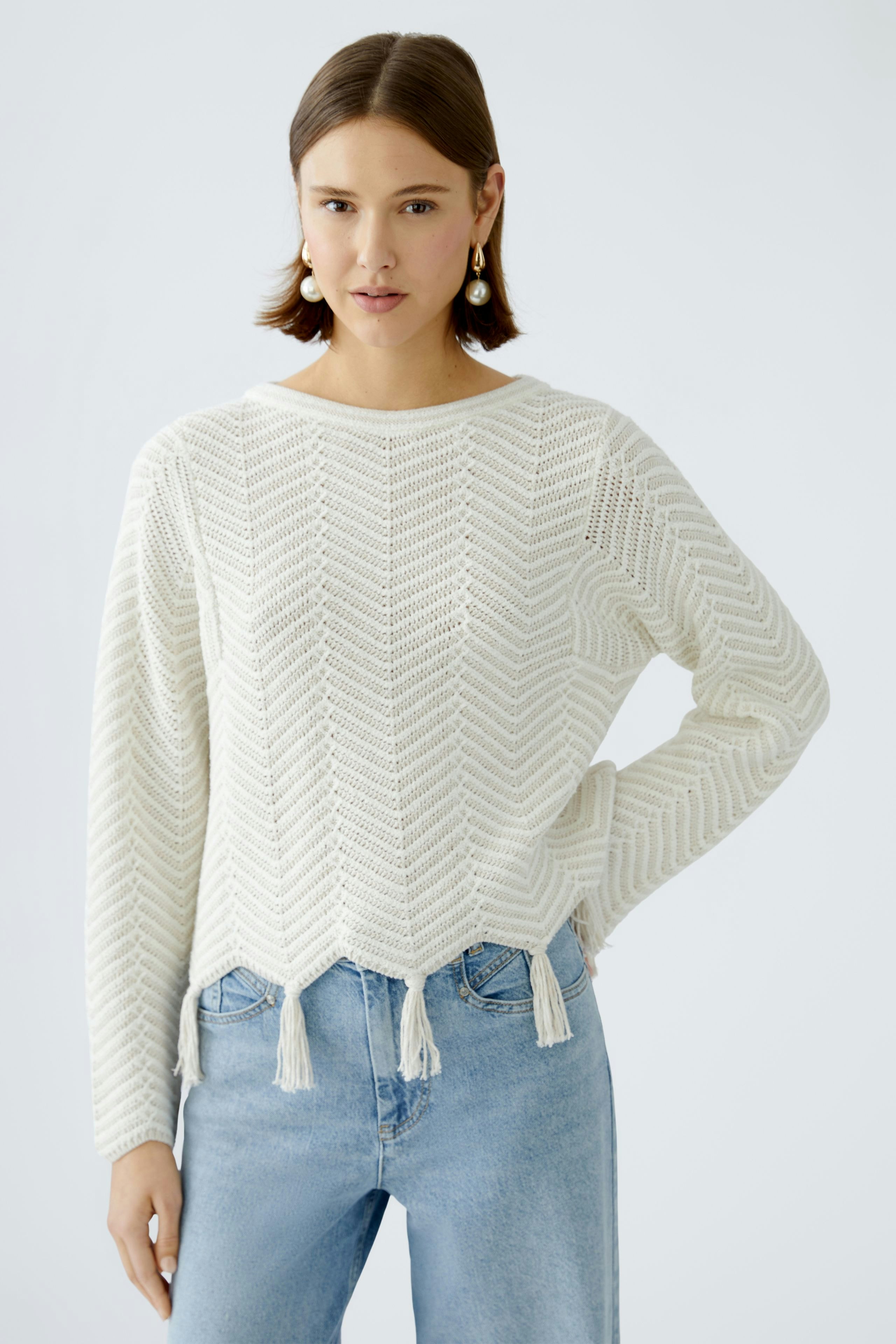 Damen-Pullover: Frau in weißem, strukturiertem Strickpullover mit Fransen und lässigen Jeans.