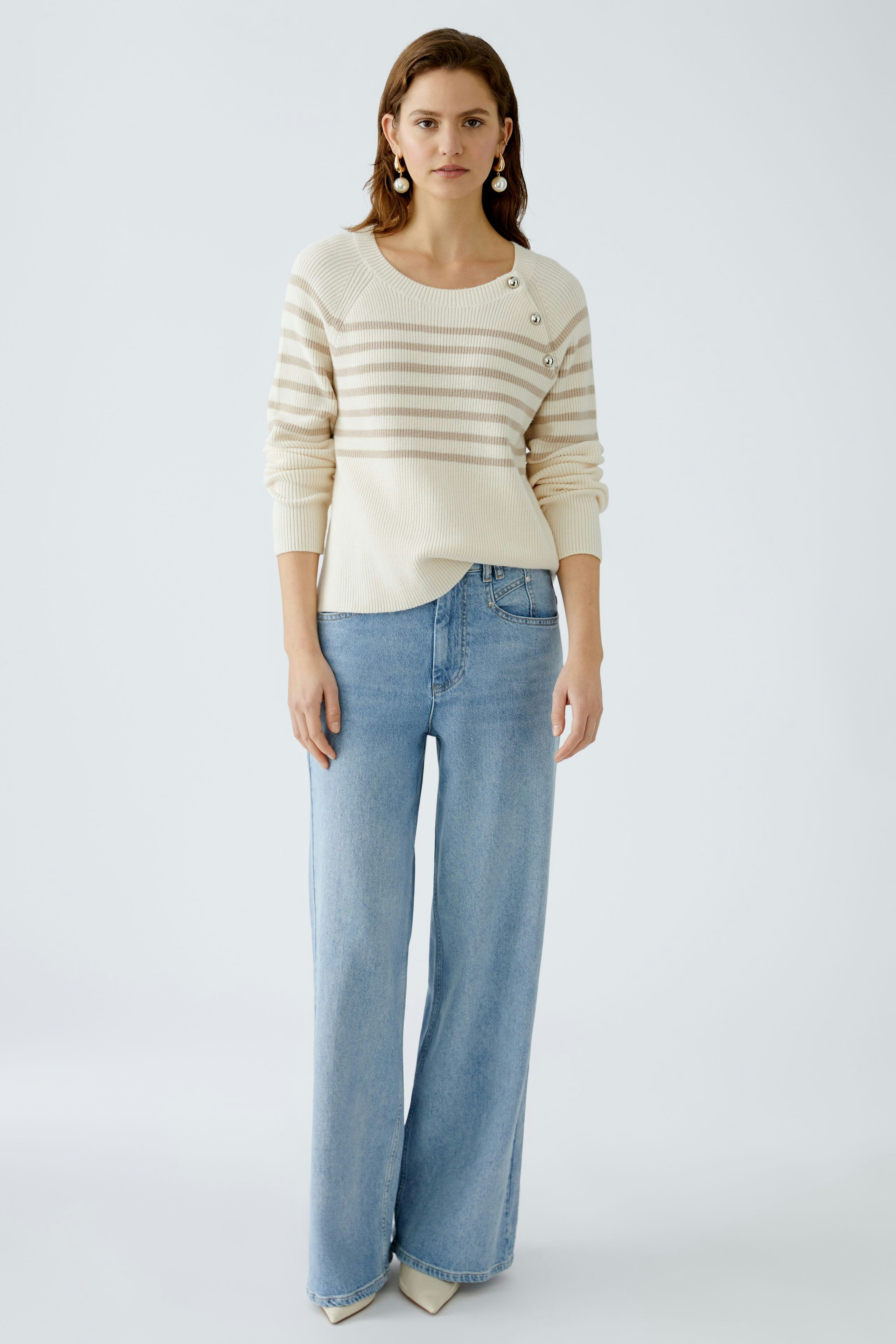 Damen-Pullover: Frau in gestreiftem, cremefarbenem Strickpullover mit Knöpfen und lässigen Jeans.
