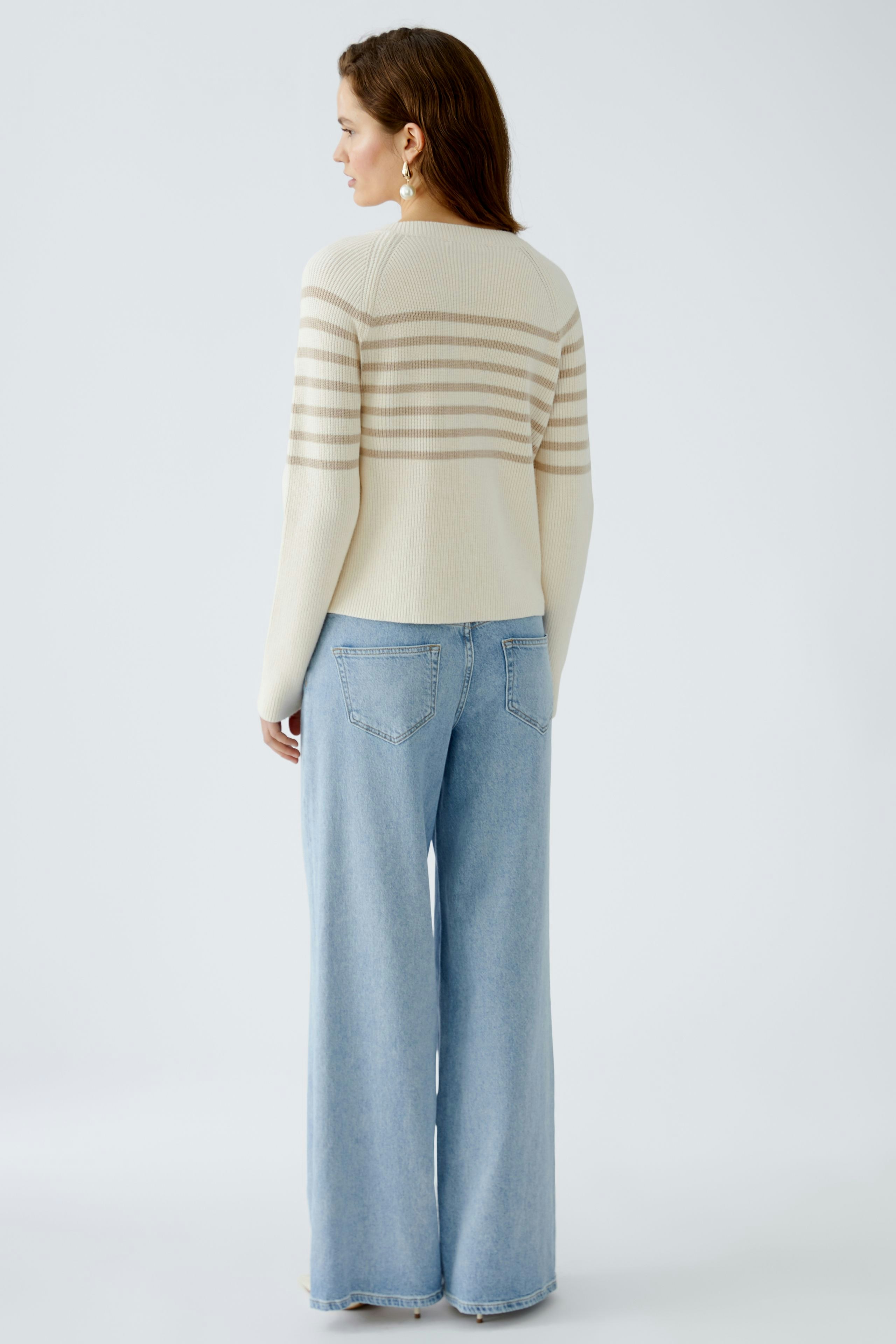 Damen-Pullover: Frau trägt einen beigen Pullover mit Streifen und lässigen Jeans.
