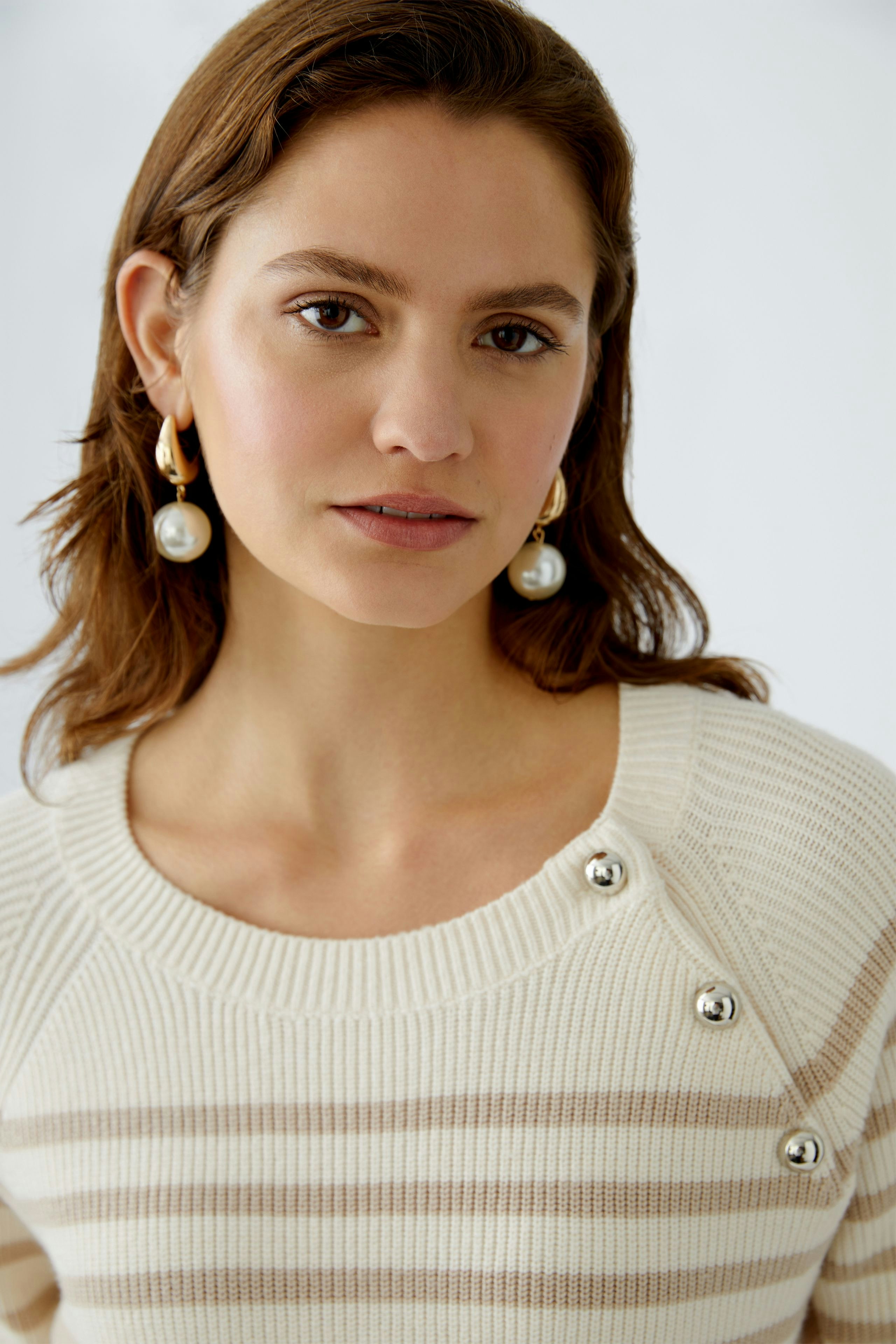 Damen-Pullover: Frau mit gestreiftem Pullover und eleganten Ohrringen lächelt freundlich.