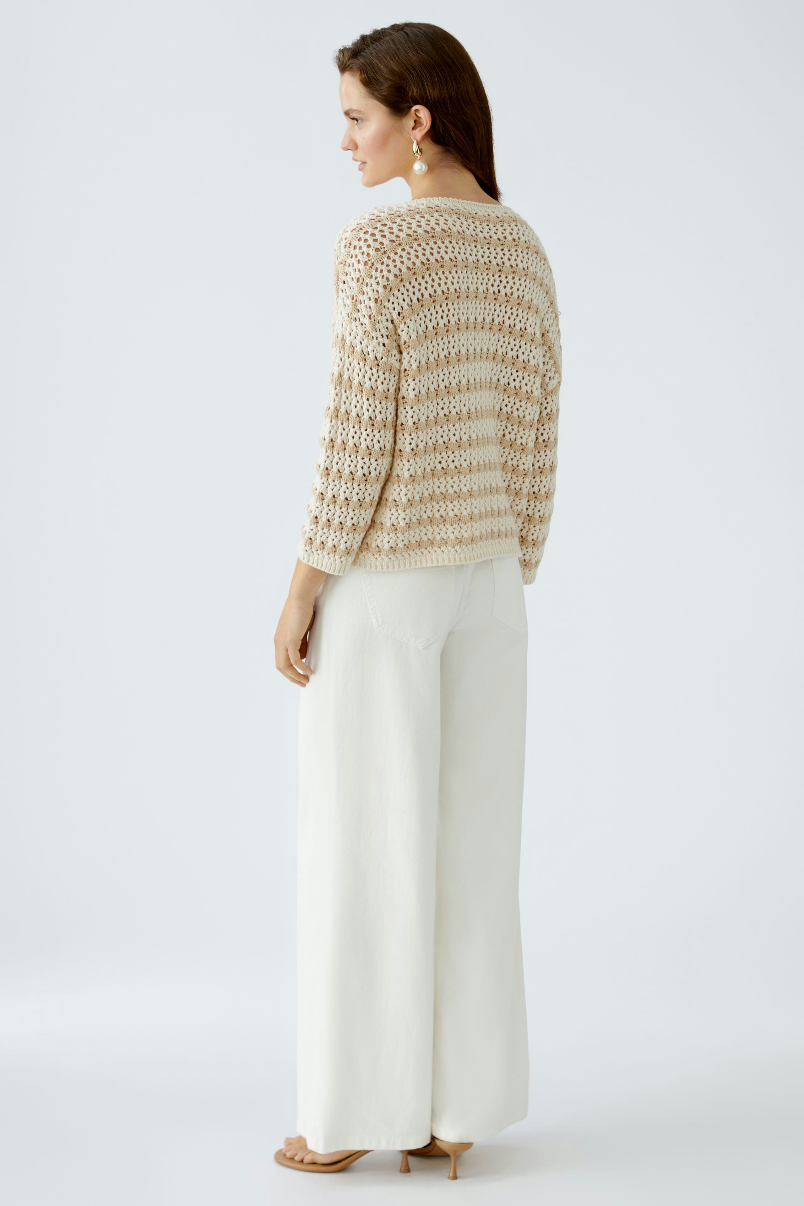 Stylish women's pullover: A woman in a light, open-knit pullover paired with wide white trousers.