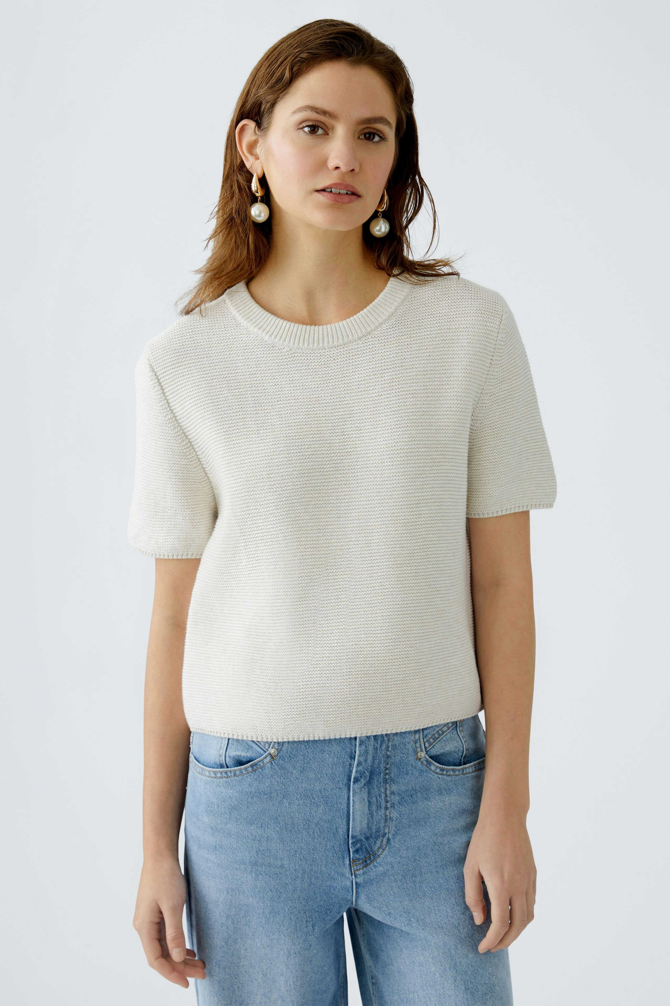 Stylish women's pullover: A woman in a light beige short-sleeve pullover paired with blue jeans.