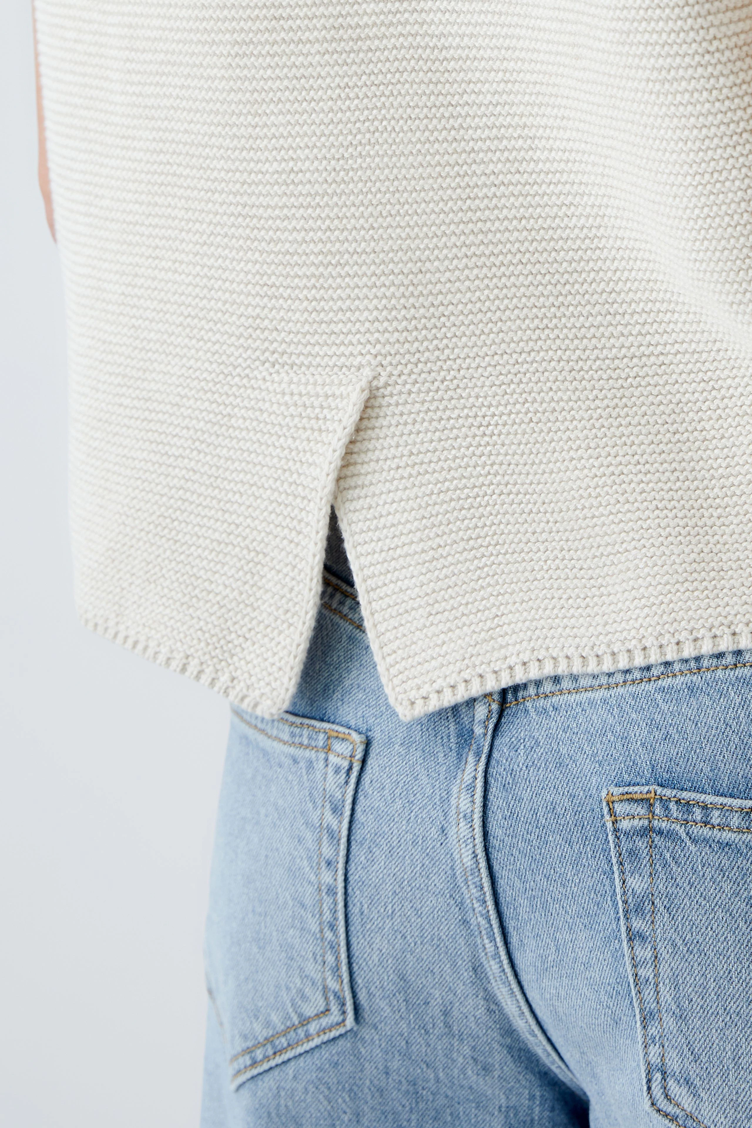 Stylish women's pullover in cream with a unique split hem, paired with casual jeans.