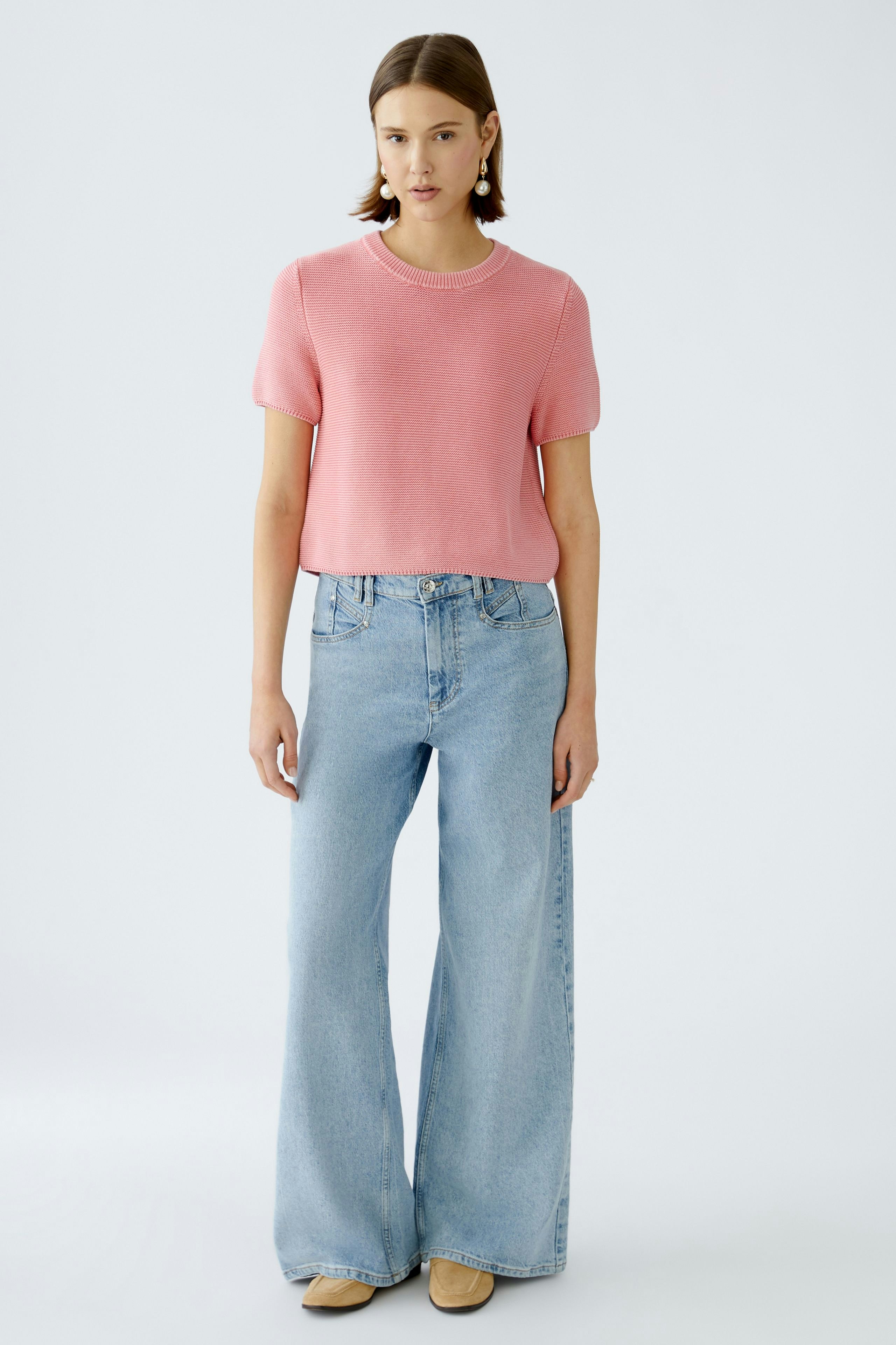 Modischer Damen-Pullover: Frau trägt einen rosa Pullover mit kurzen Ärmeln und lässigen Jeans.