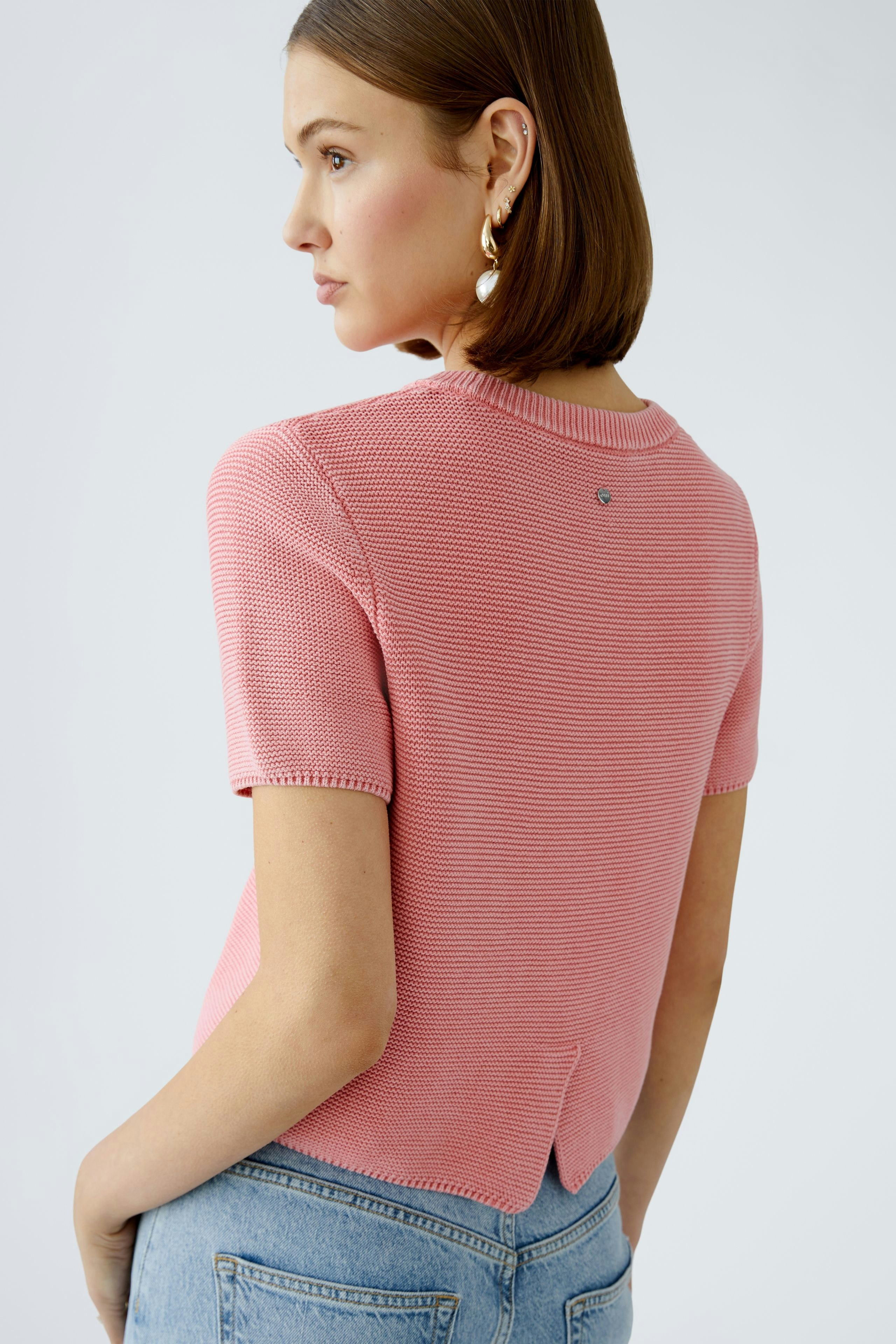 Damen-Pullover: Frau in rosa, kurzärmligem Strickpullover mit feinen Streifen und seitlichem Schlitz.