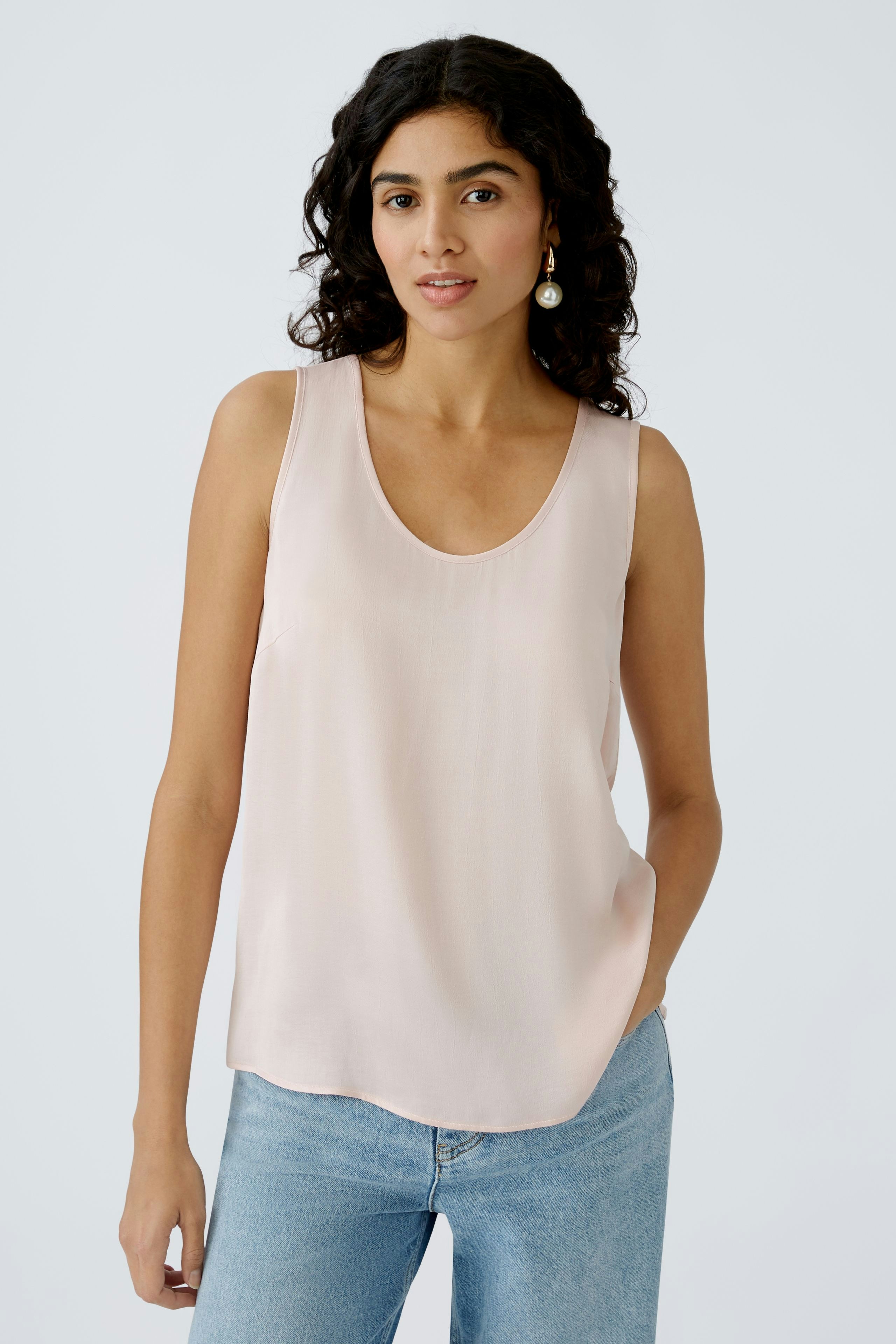 Elegant women's top: A woman in a light pink sleeveless top paired with casual jeans.
