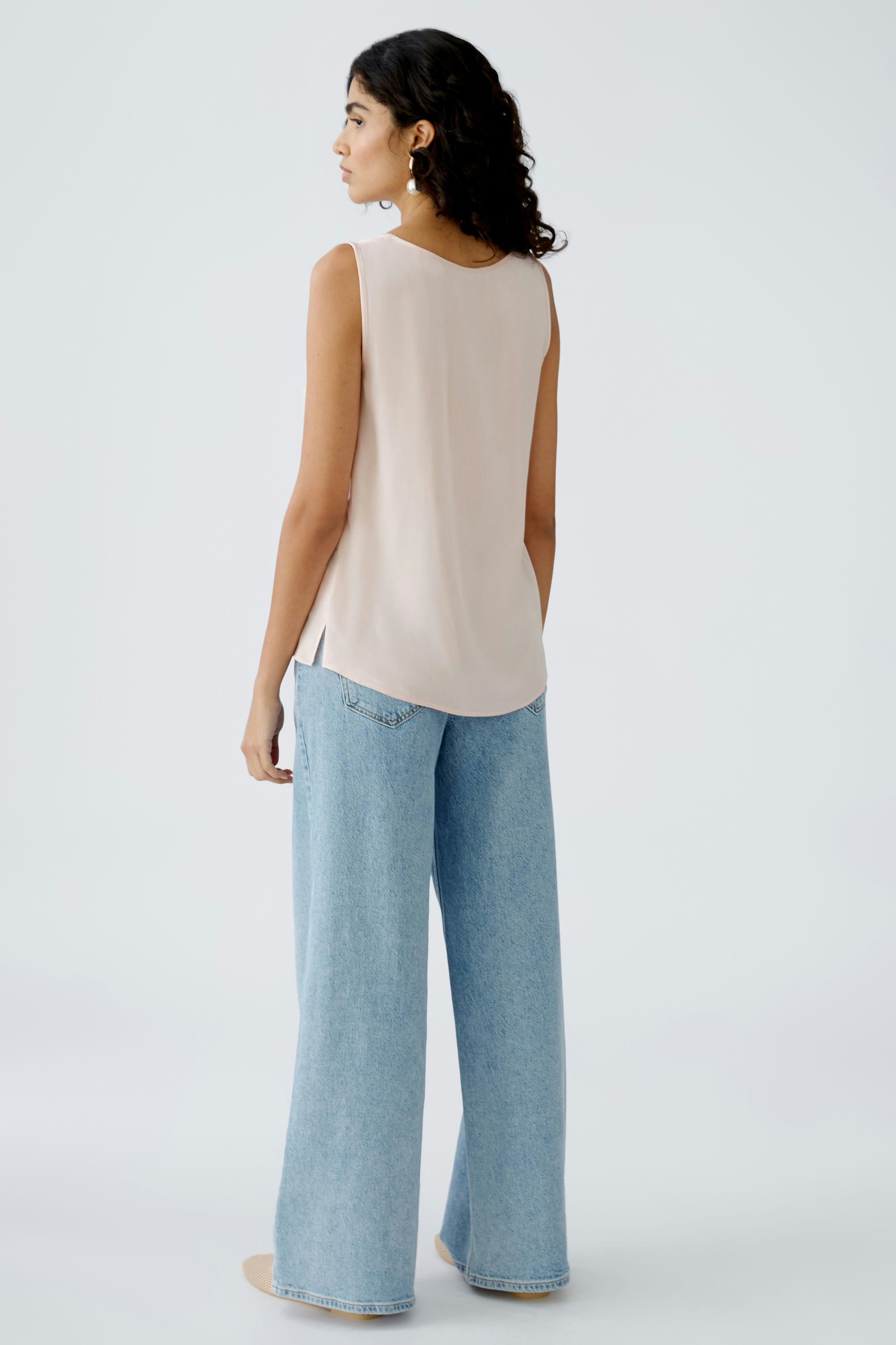 Elegant women's top: A woman in a light beige sleeveless top paired with wide-leg jeans.