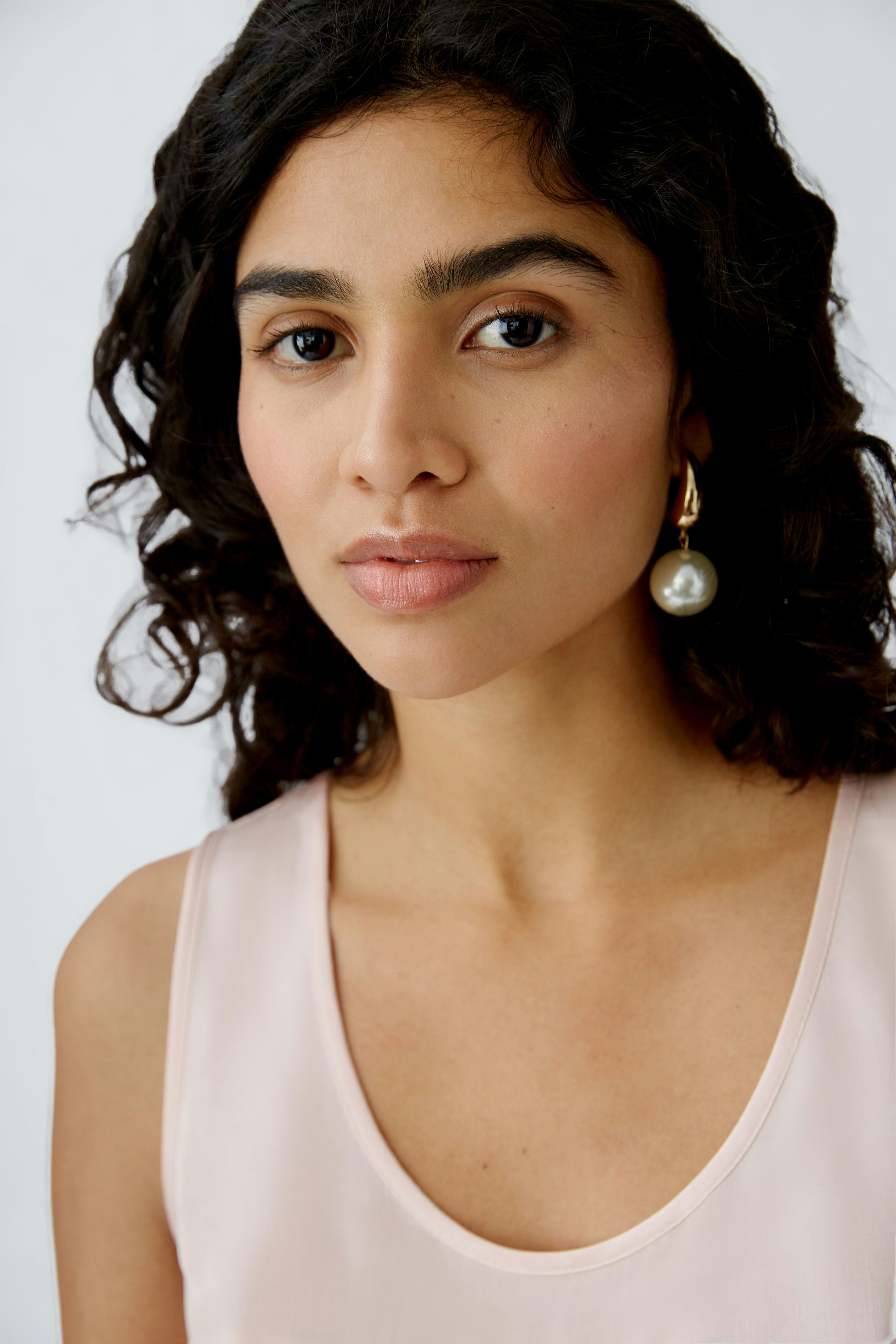 Elegant women's top: A woman with curly hair wears a soft pink sleeveless top, exuding a chic and modern vibe.