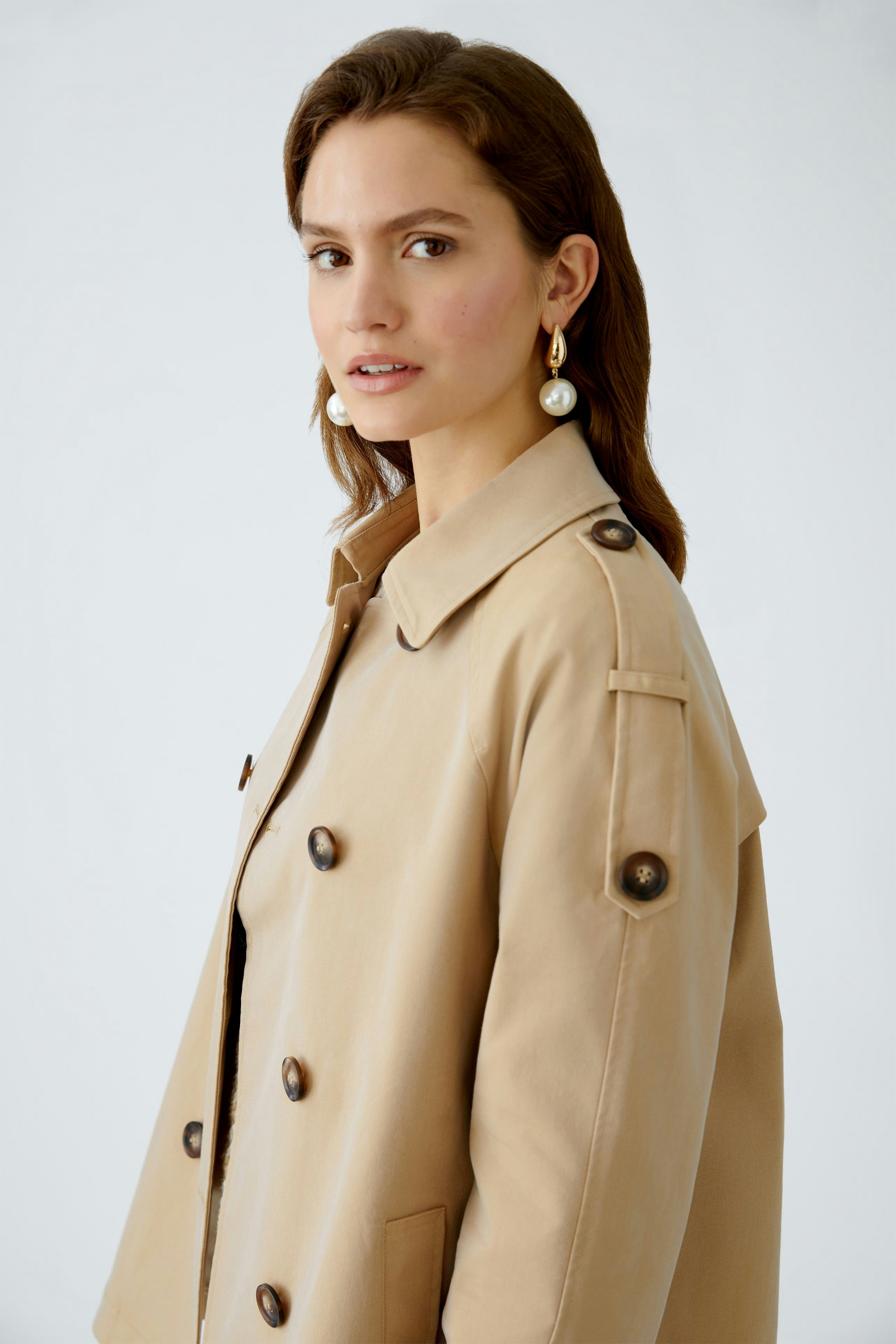 Beige Outdoorjacke: Junge Frau trägt eine elegante, knielange Jacke mit großen Knöpfen und lässigem Schnitt.