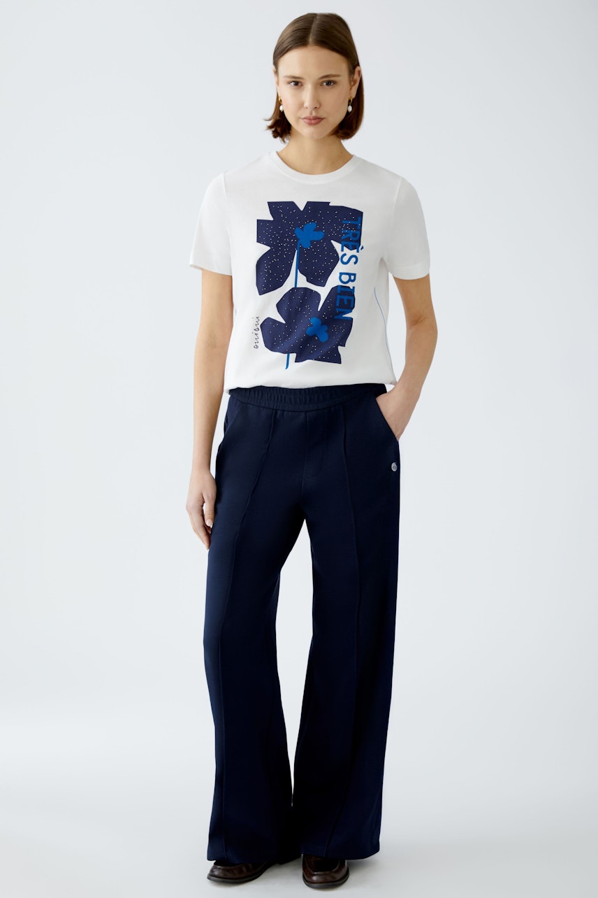 Stylish women's T-shirt: A woman in a white tee with a blue graphic design, paired with navy trousers.