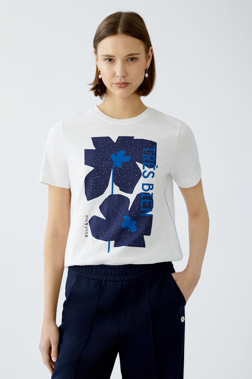 Stylish women's T-shirt: A woman in a white tee with blue floral print and text, exuding casual elegance.