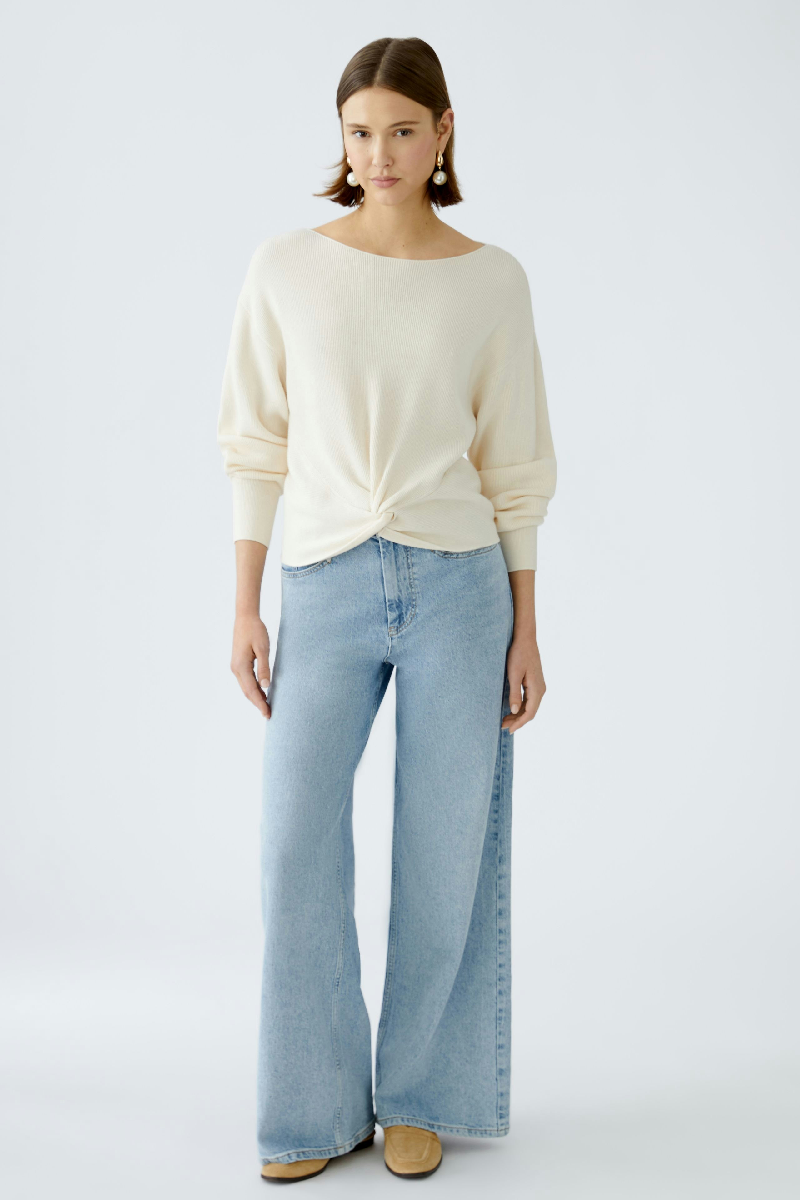 Damen-Pullover: Junge Frau in einem hellen, lässigen Pullover mit Knoten-Detail und weiten Jeans.