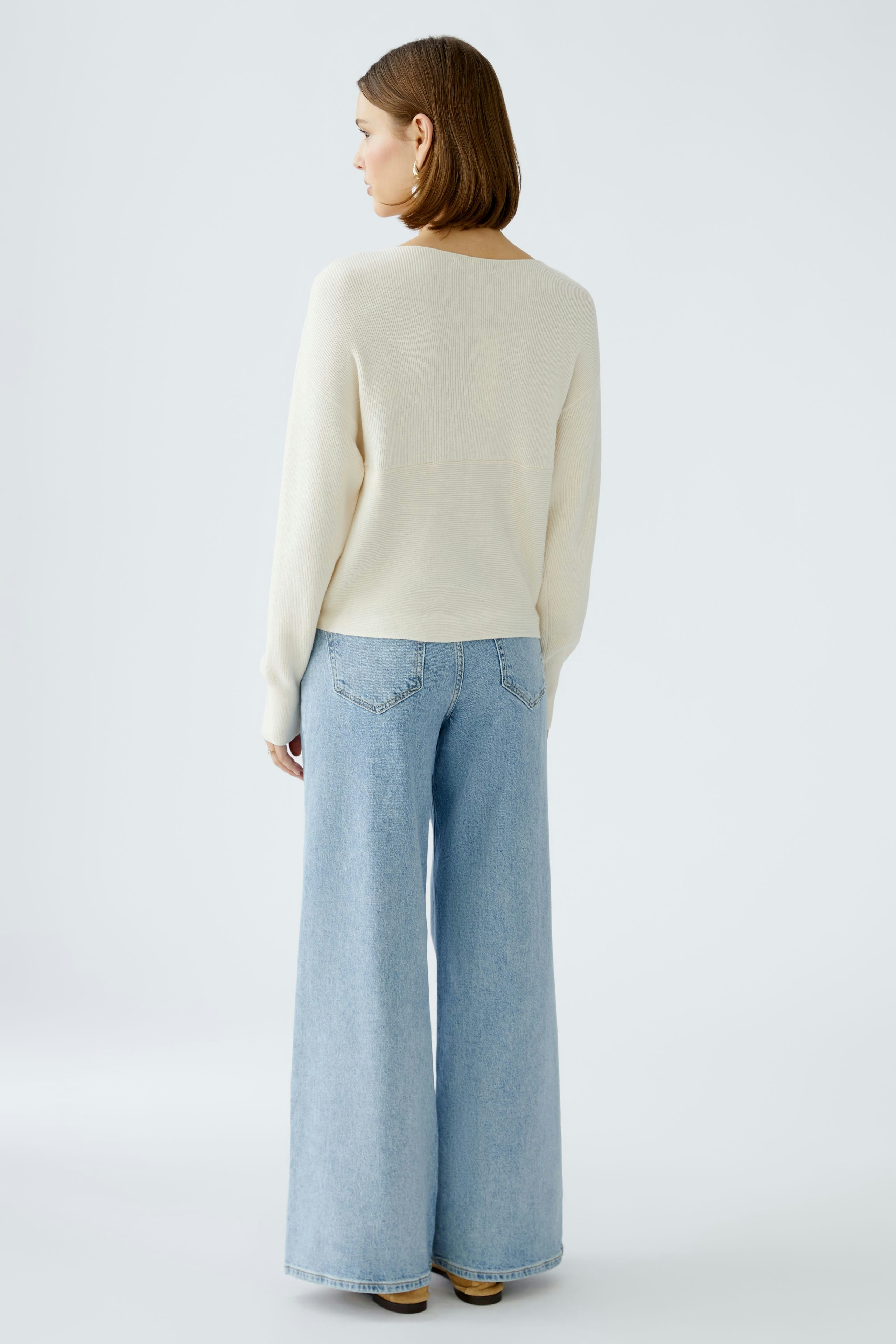 Eleganter Damen-Pullover in Cremefarbe, lässig kombiniert mit weiten Jeans, von hinten fotografiert.