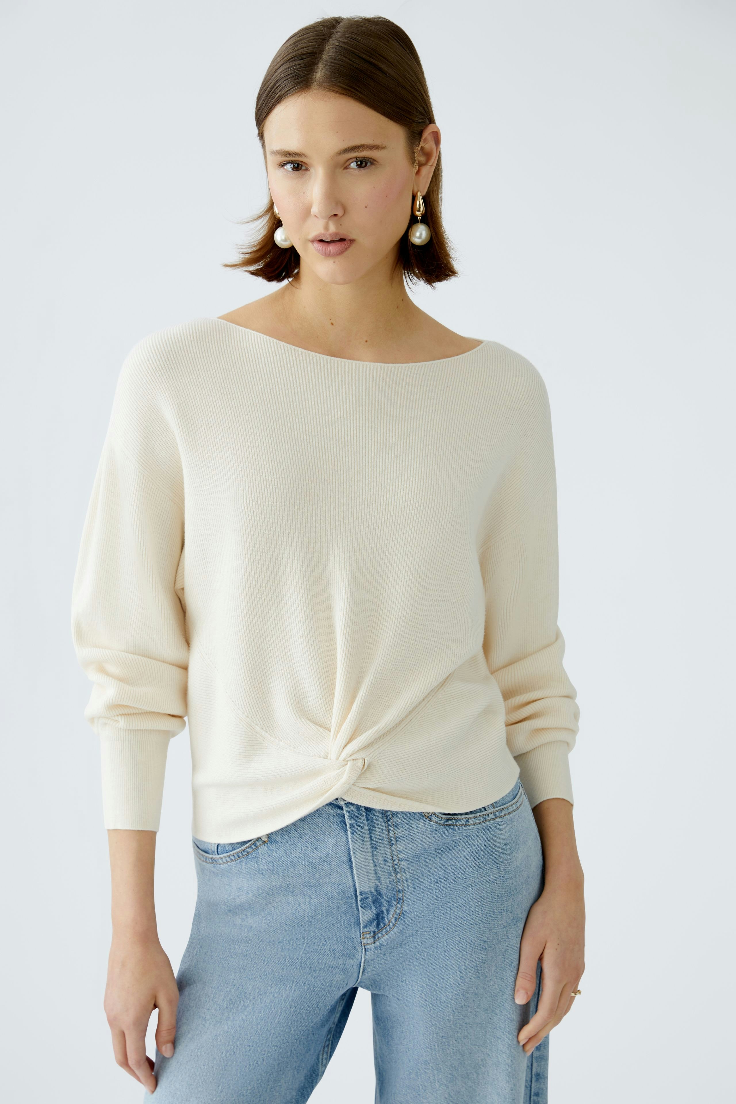 Eleganter Damen-Pullover in Creme mit lässigem Knoten-Detail, kombiniert mit Jeans.