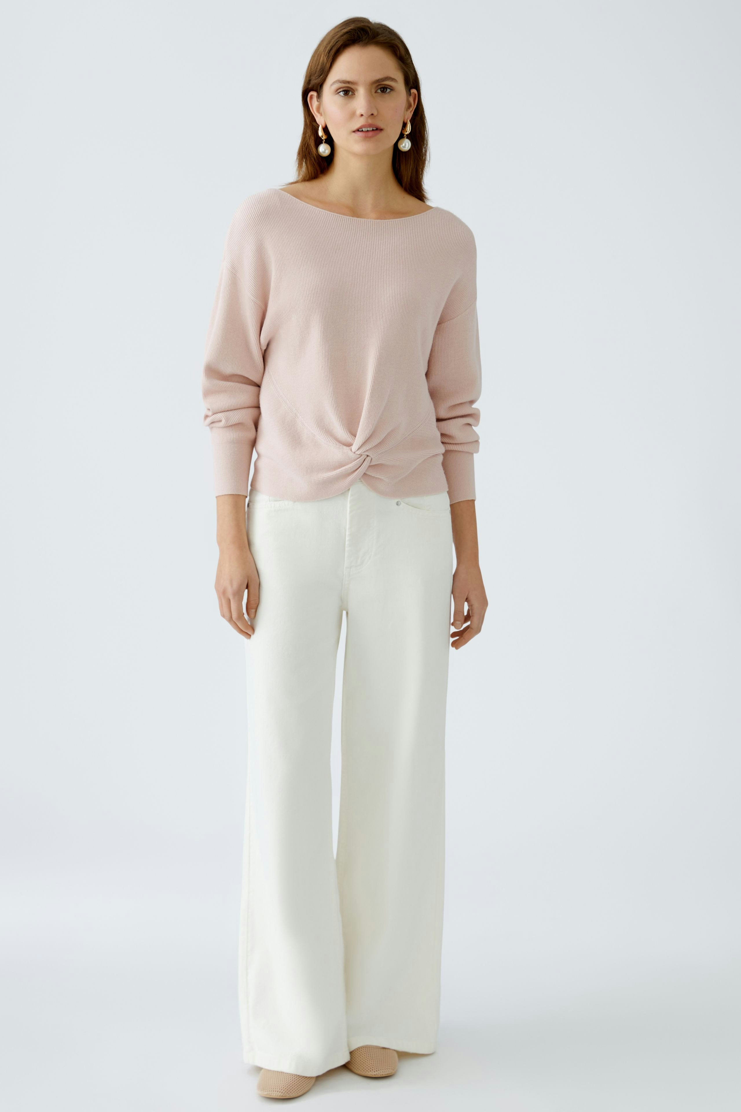 Stylish women's pullover: A woman in a soft pink pullover with a knotted front, paired with wide-leg pants.