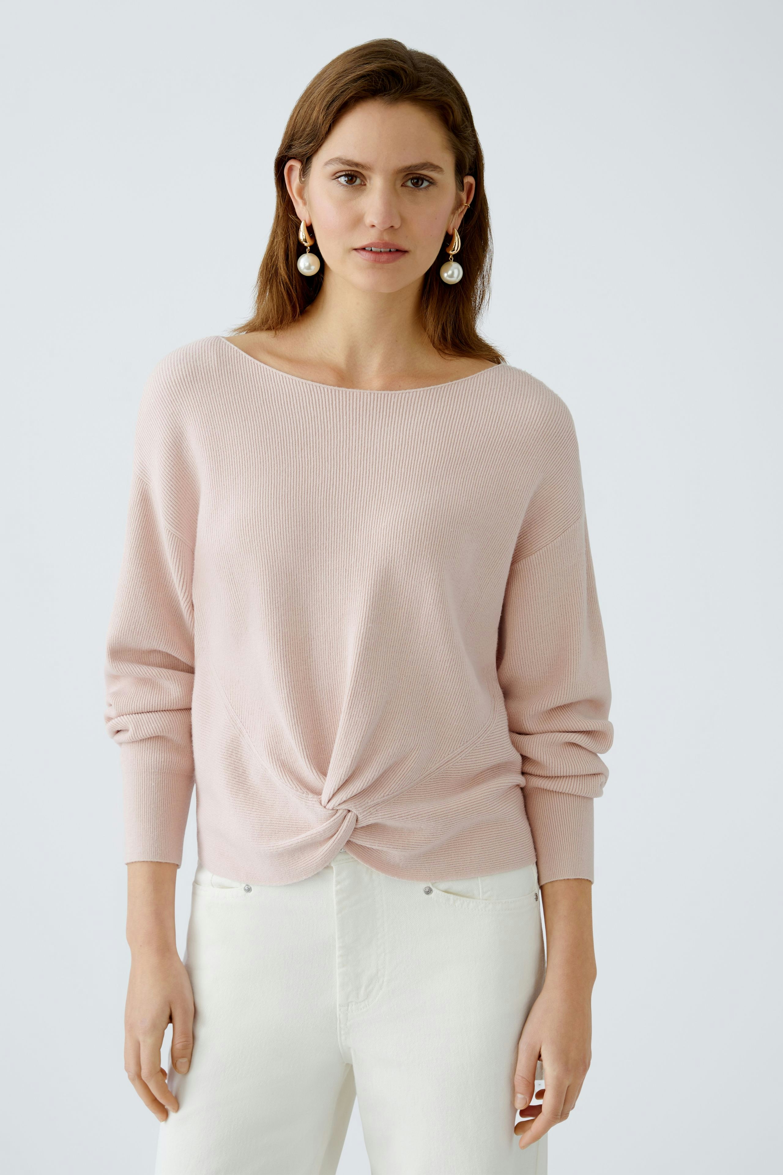 Stylish women's pullover: A woman in a soft pink pullover with a knot detail, paired with white pants.