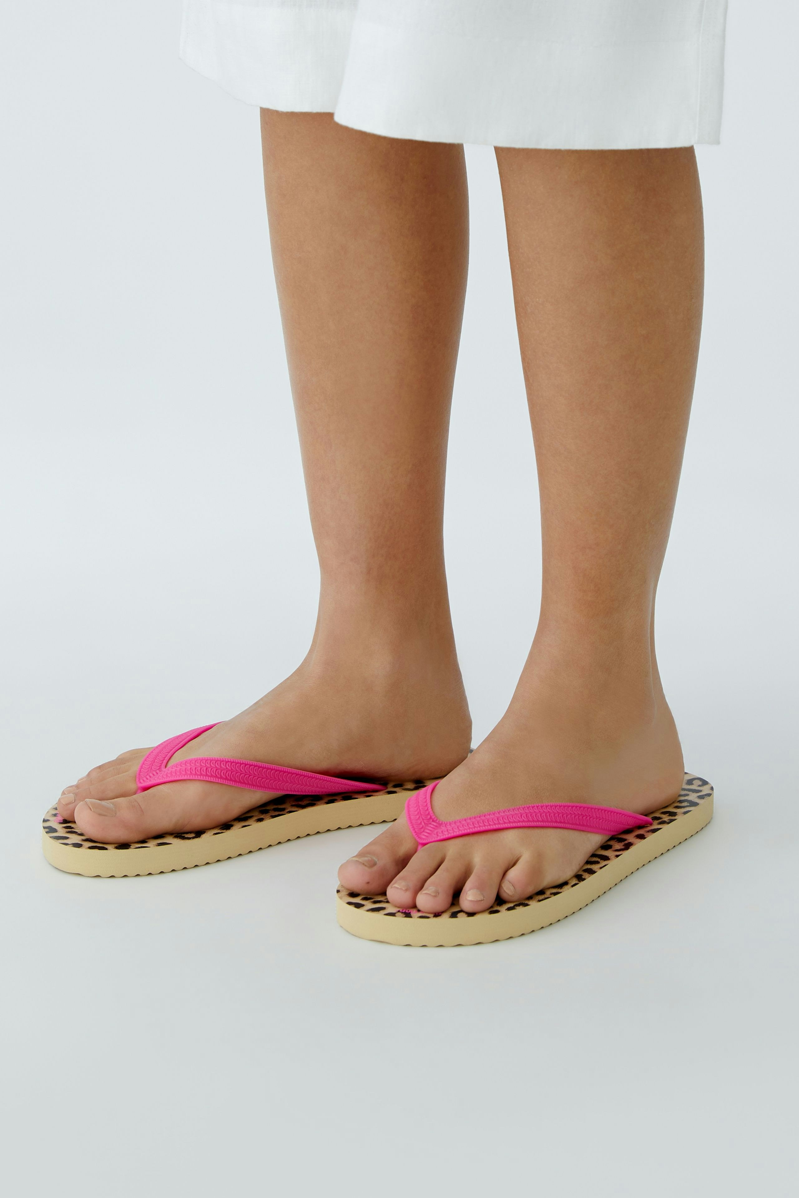 Bequeme Damen-Sandalen: Frau trägt pinke Flip-Flops mit Leopardenmuster und genießt den Sommer.