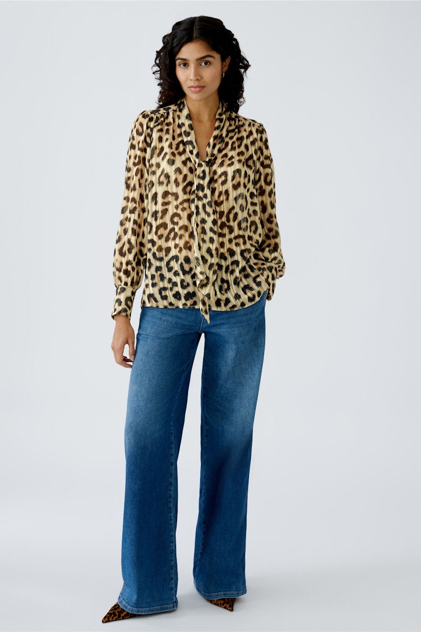 Leopardenbluse: Frau trägt eine elegante, transparente Bluse mit Leopardenmuster und lässigen Jeans.