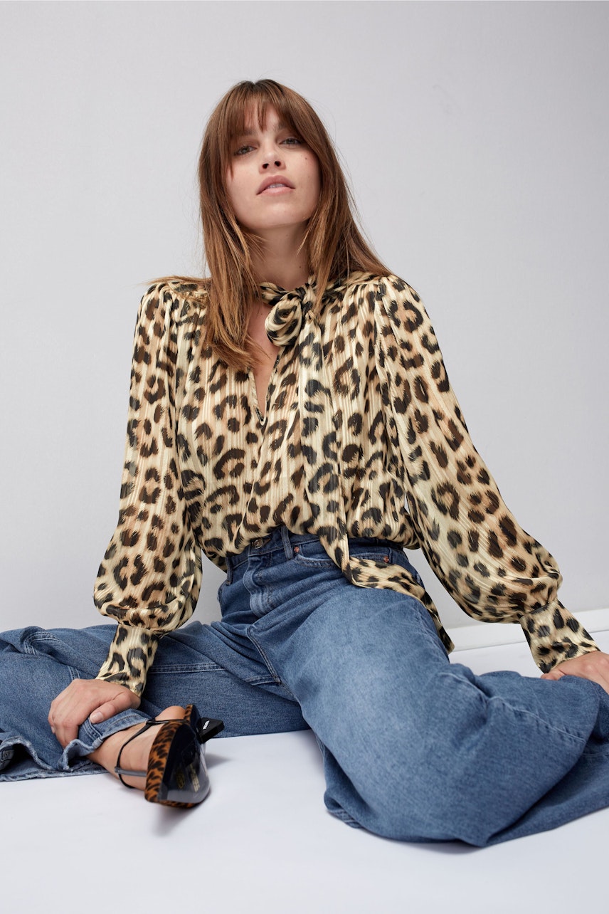 Leopardenbluse: Frau in eleganter Bluse mit Leoprint und lässigen Jeans sitzt entspannt.