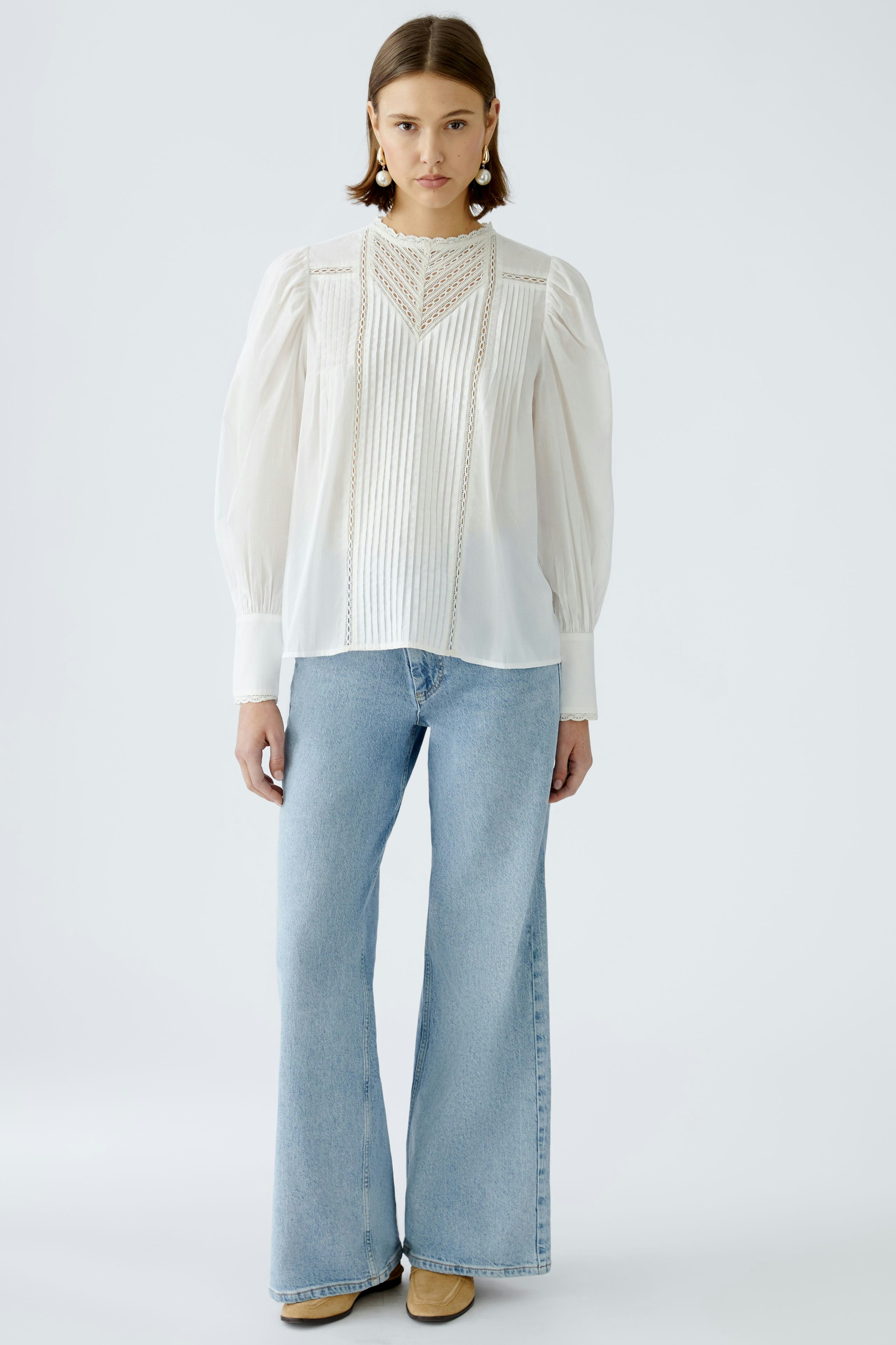 Elegante Damen-Bluse: Frau in weißer Bluse mit feinen Details und lässigen Jeans.