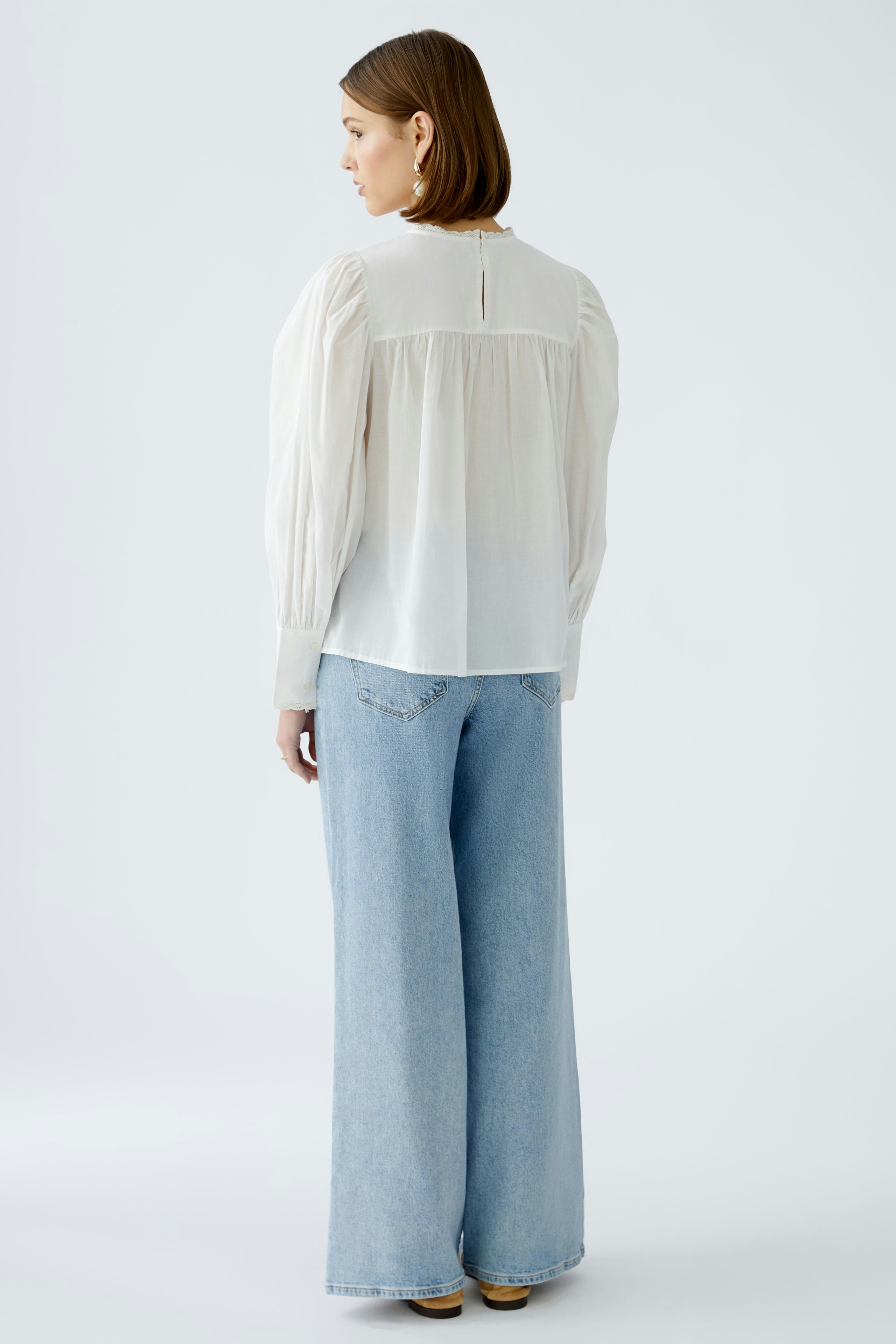 Elegante Damen-Bluse: Frau in einer hellen Bluse mit Puffärmeln und lässigen Jeans von hinten.