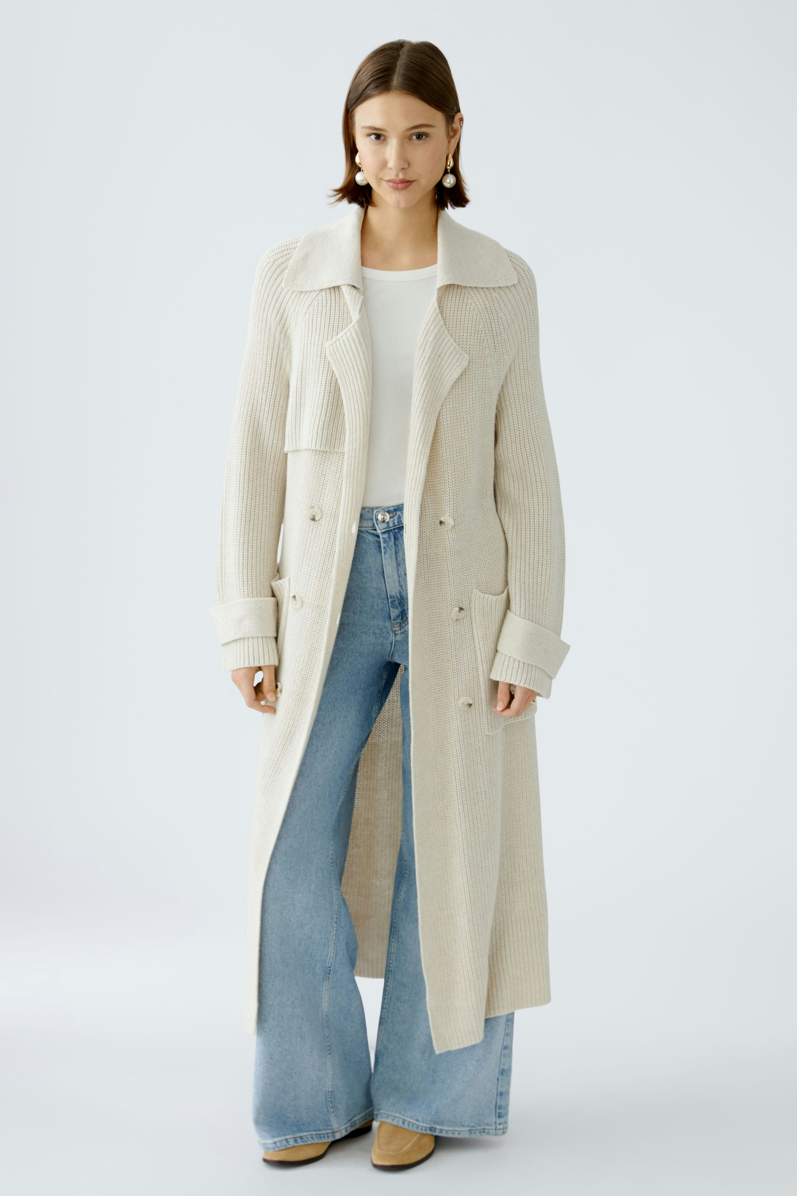Elegant women's cardigan: A woman in a cream ribbed cardigan over a white top and wide-leg jeans.