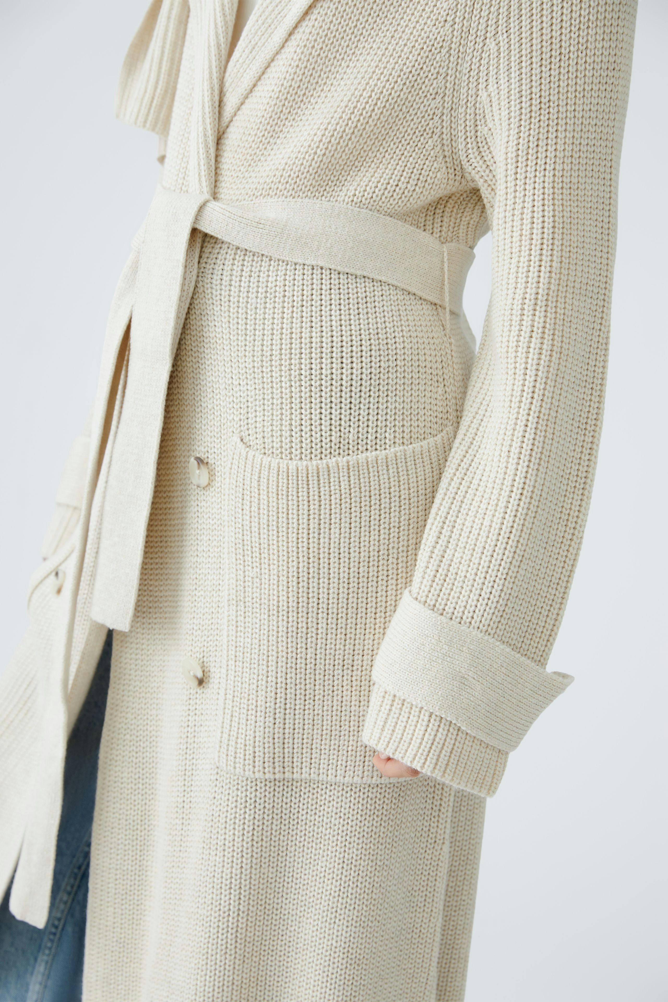 Stylish women's cardigan: A woman in a beige knitted cardigan with a belt and pockets.