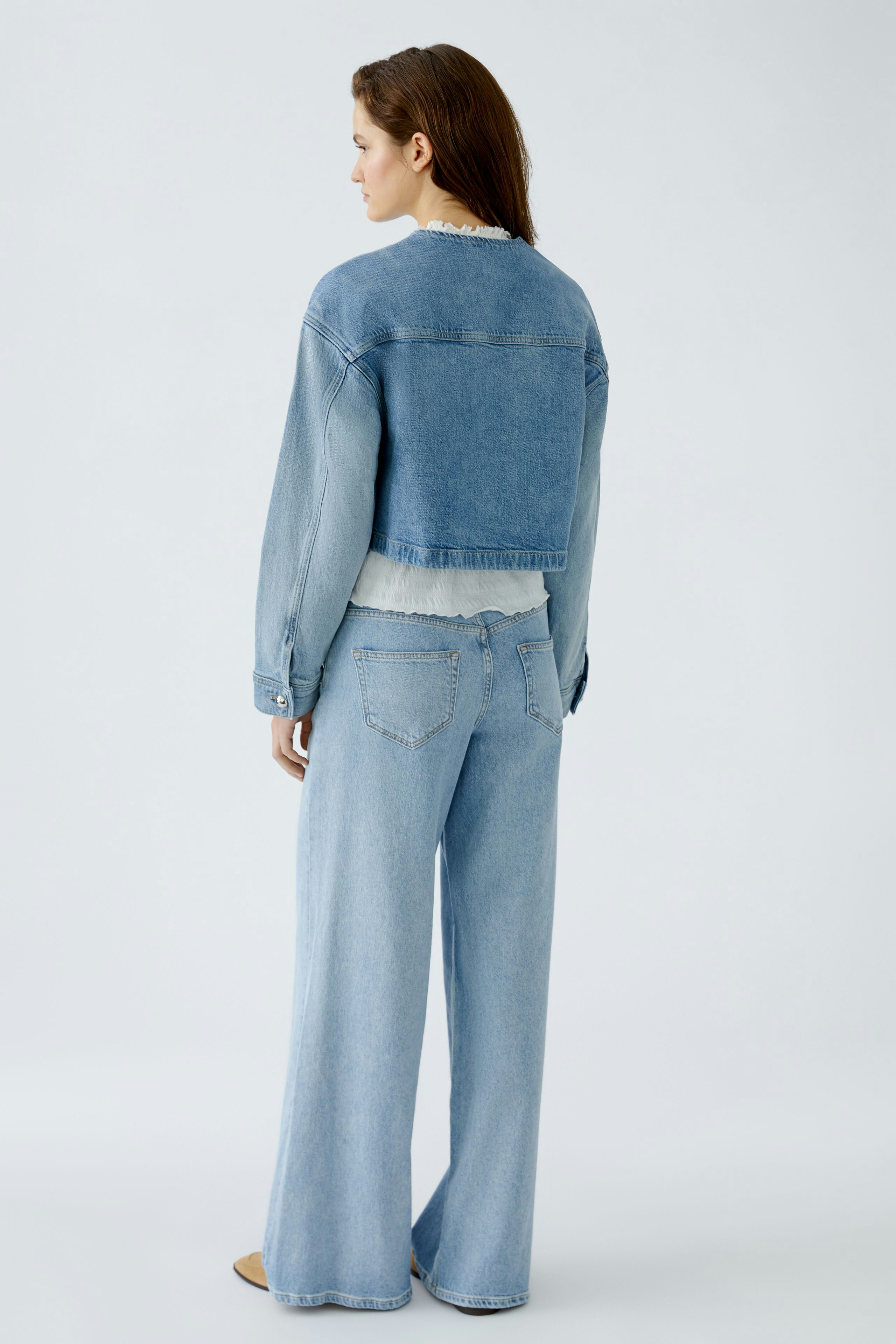 Damen-Jeansjacke: Frau in blauer Jeansjacke mit lässigem Schnitt und weiten Jeans im minimalistischen Look.