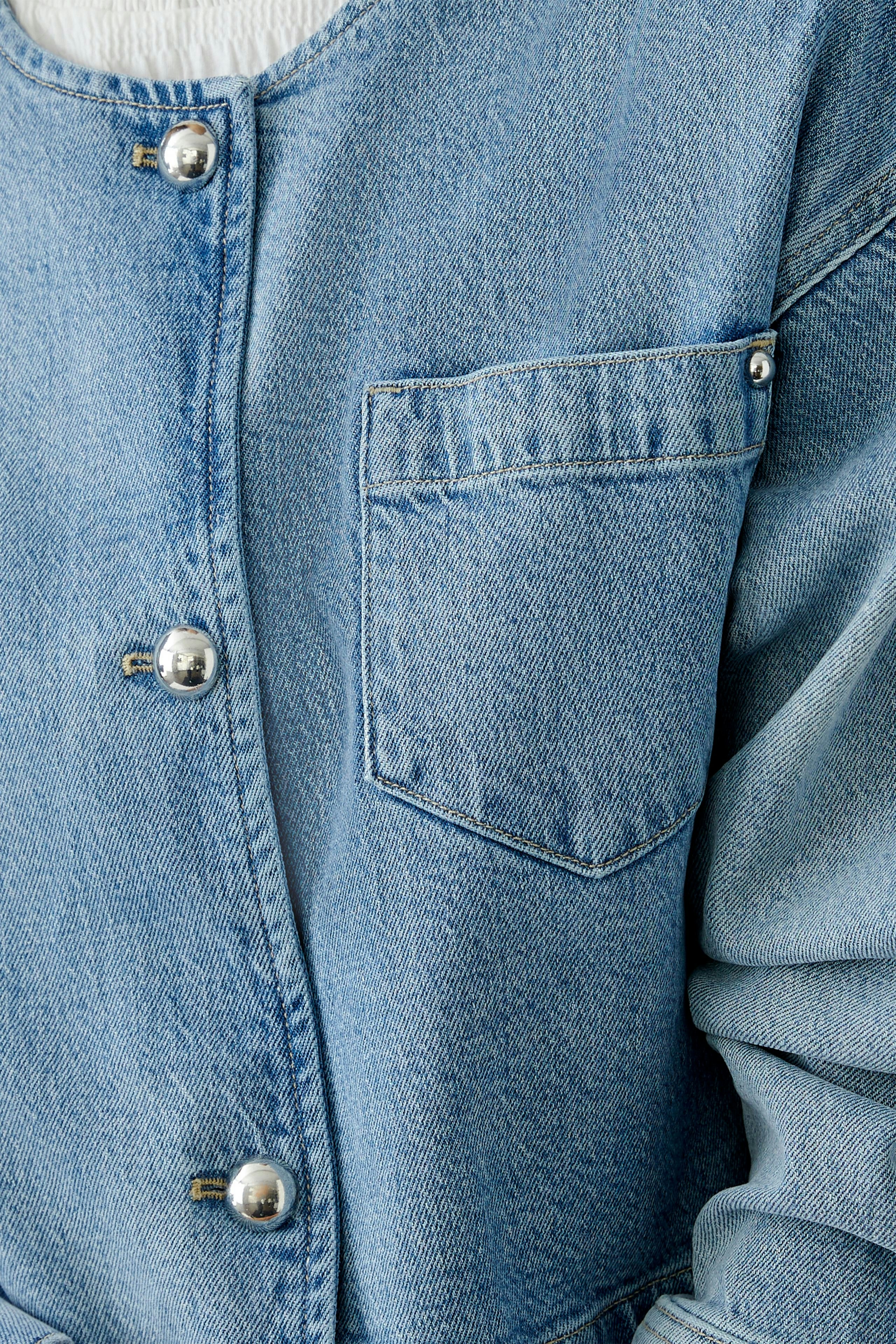 Moderne Jeansjacke: Detailaufnahme einer blauen Jeansjacke mit Druckknöpfen und Brusttasche.