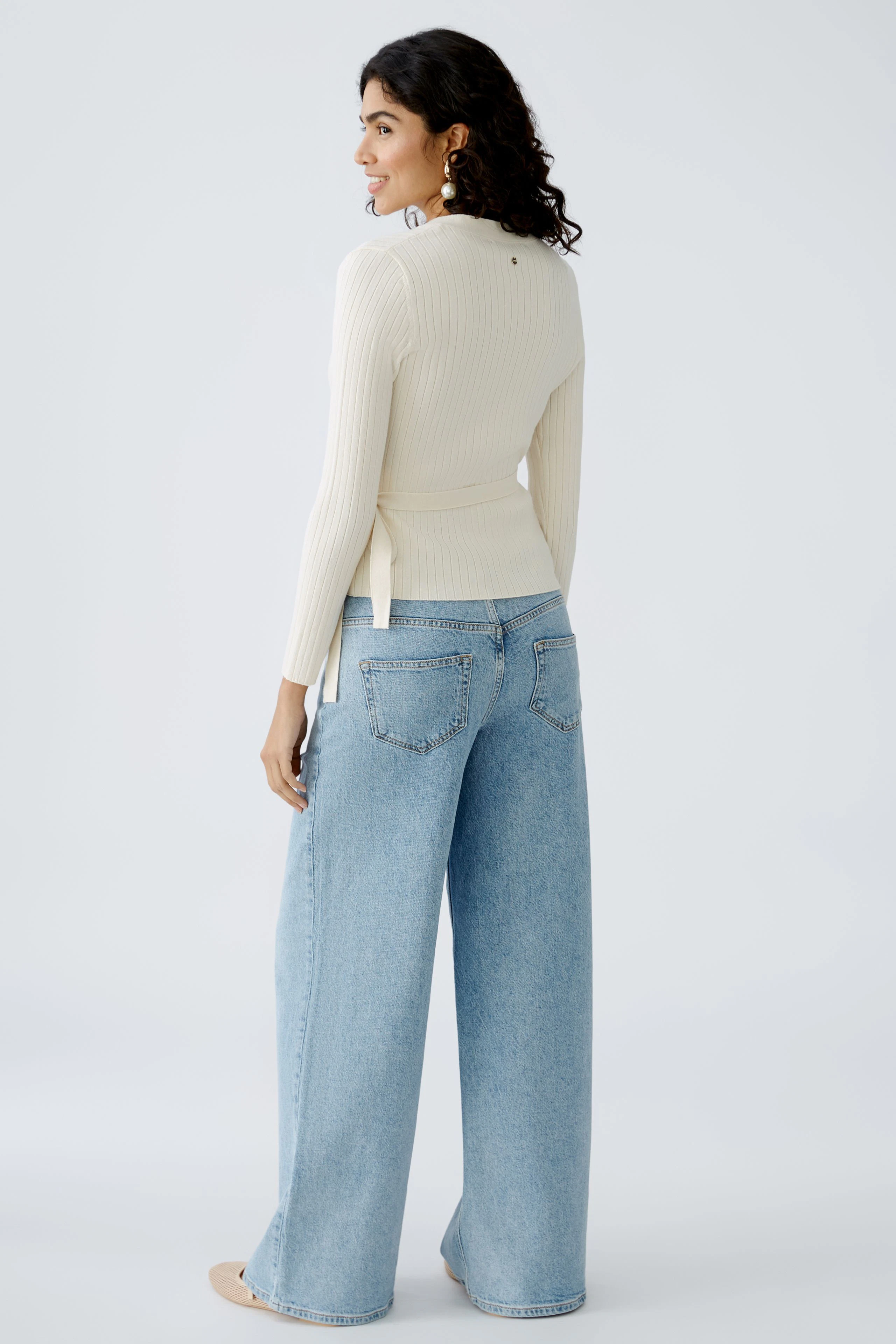 Elegante Damen-Strickjacke: Frau in cremefarbener Strickjacke mit lässigen Jeans von hinten.