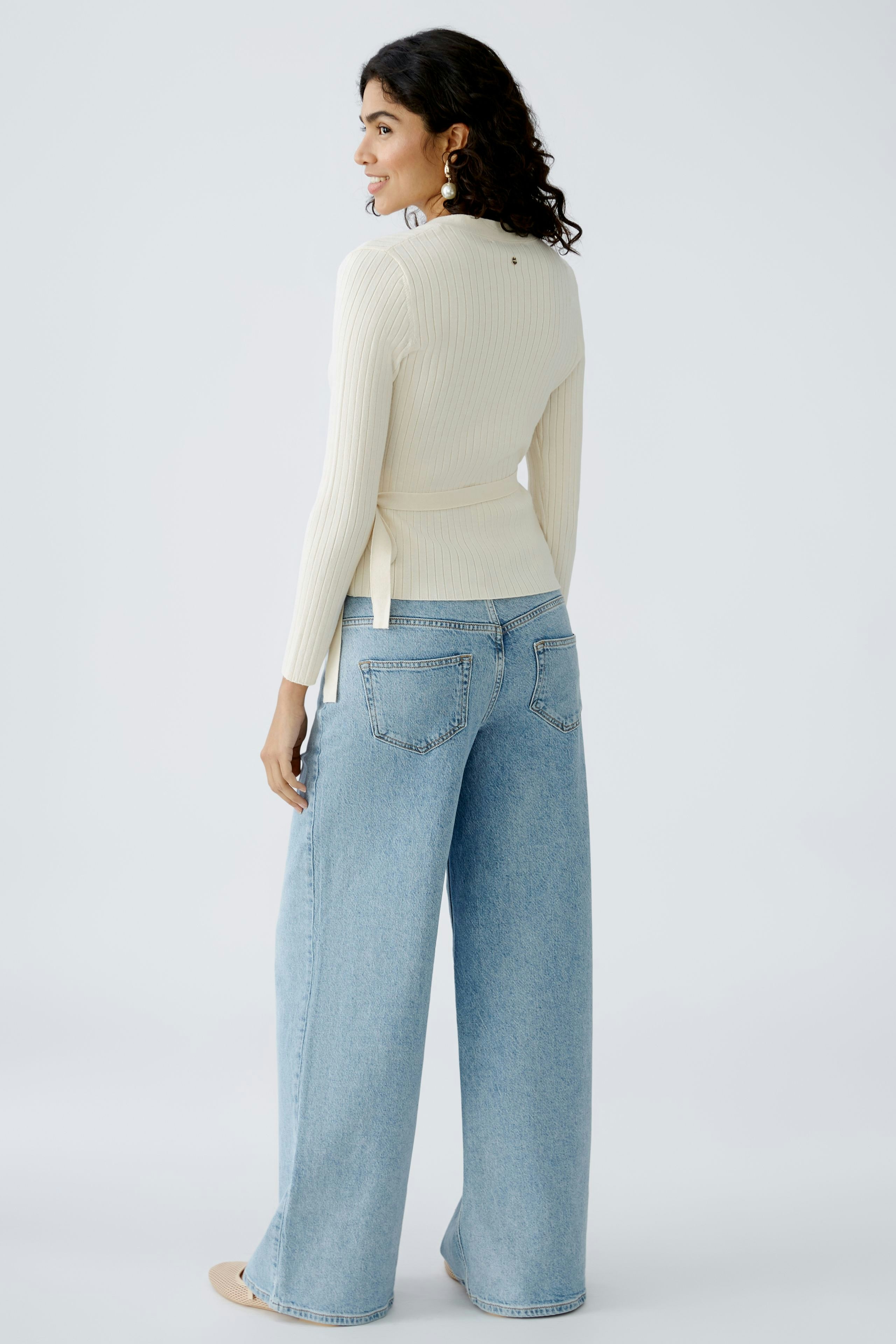 Elegante Damen-Strickjacke: Frau in cremefarbener Strickjacke mit lässigen Jeans von hinten.