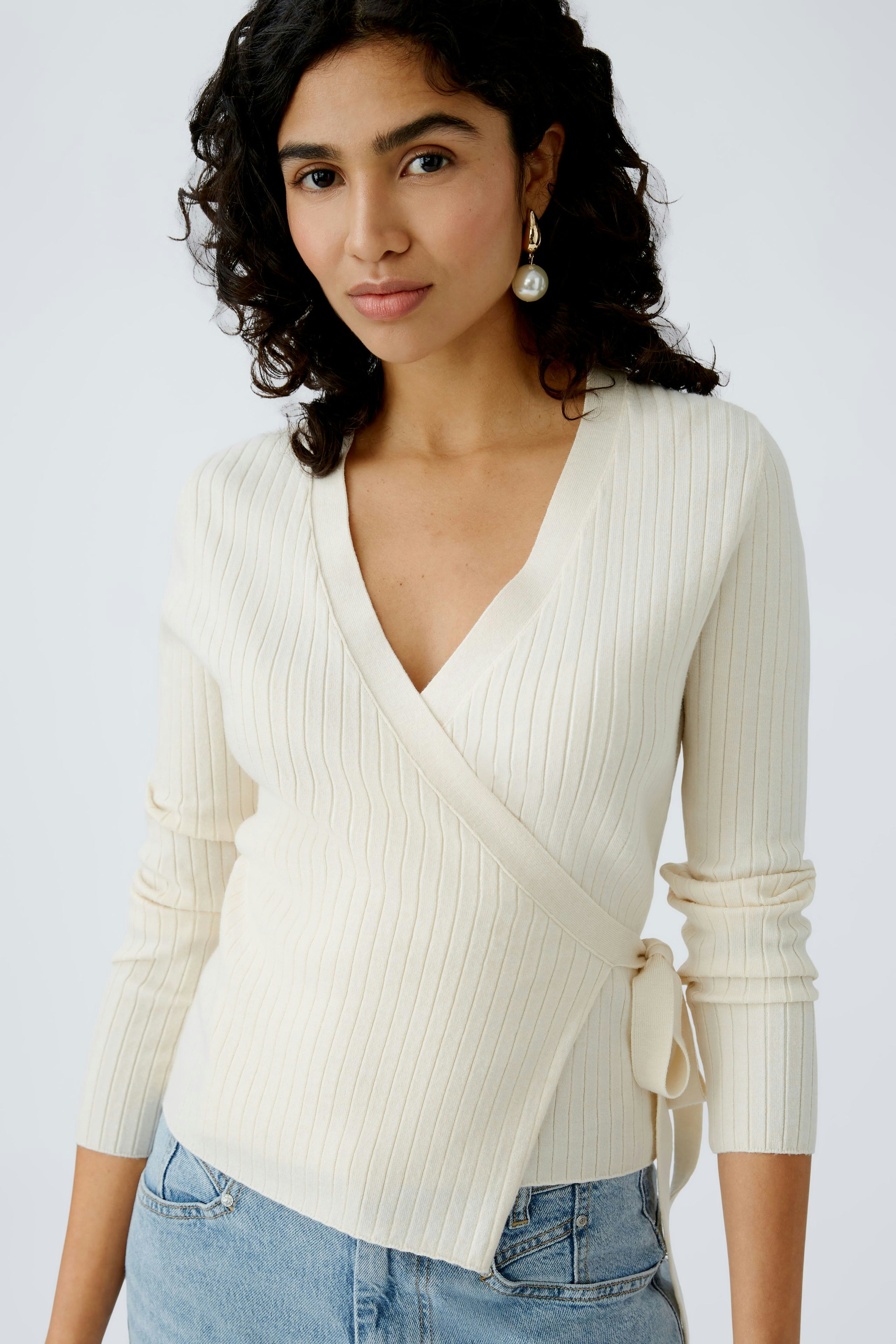 Elegante Damen-Strickjacke: Frau in cremefarbener, taillierter Strickjacke mit V-Ausschnitt und Bindeband.