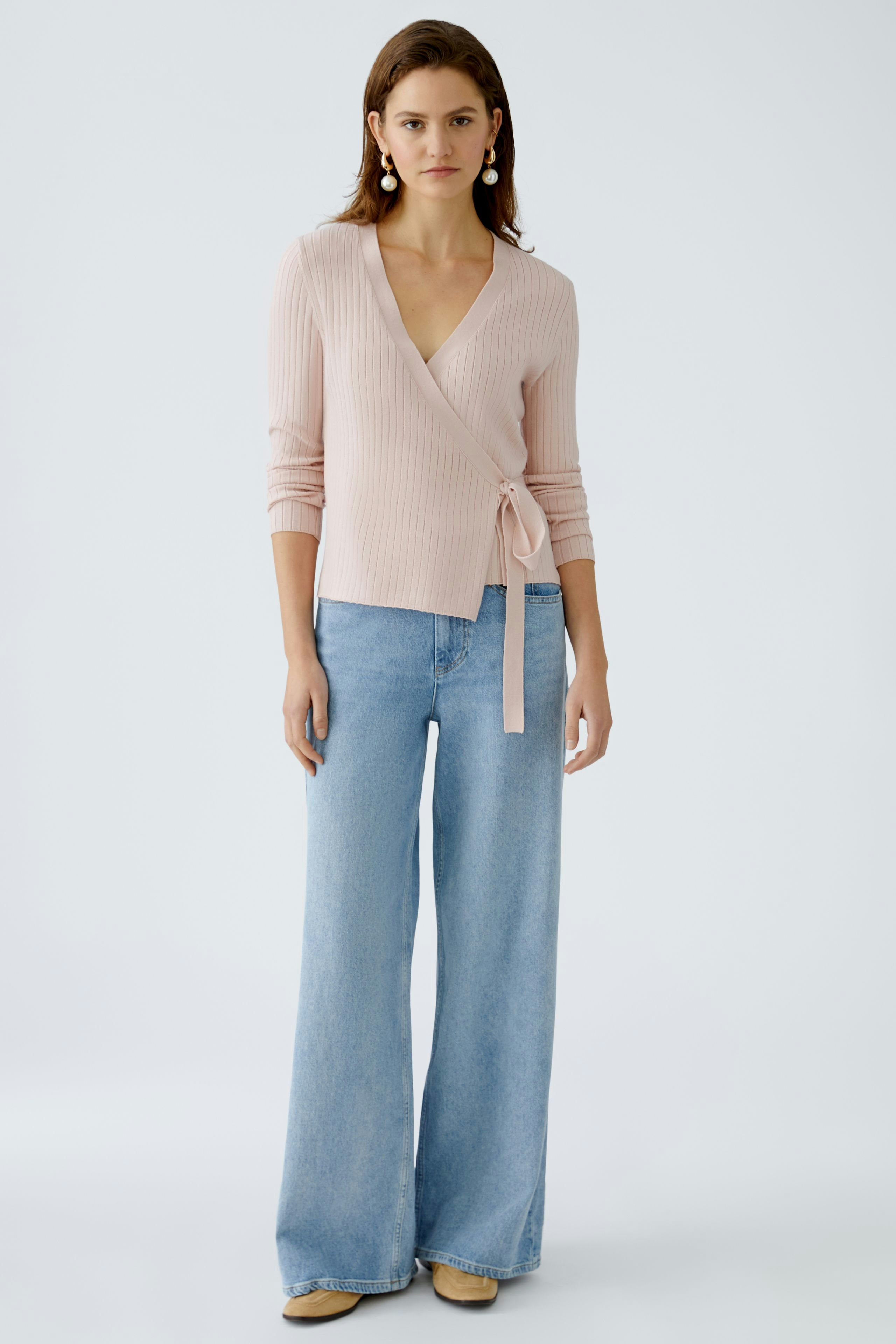 Elegant women's cardigan: A woman in a soft pink wrap cardigan paired with wide-leg jeans.