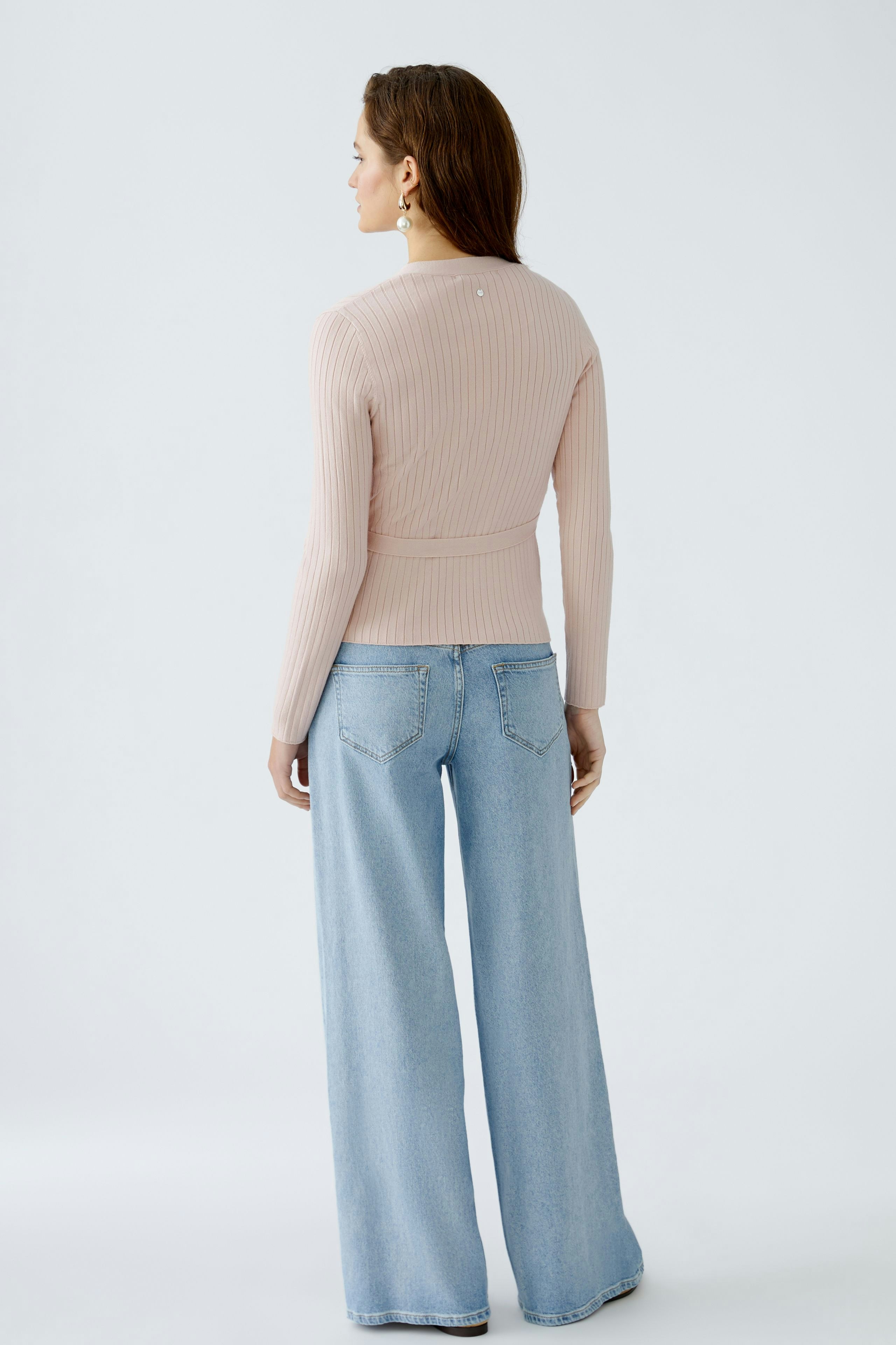 Stylish women's cardigan: A woman in a soft pink ribbed cardigan paired with wide-leg jeans.