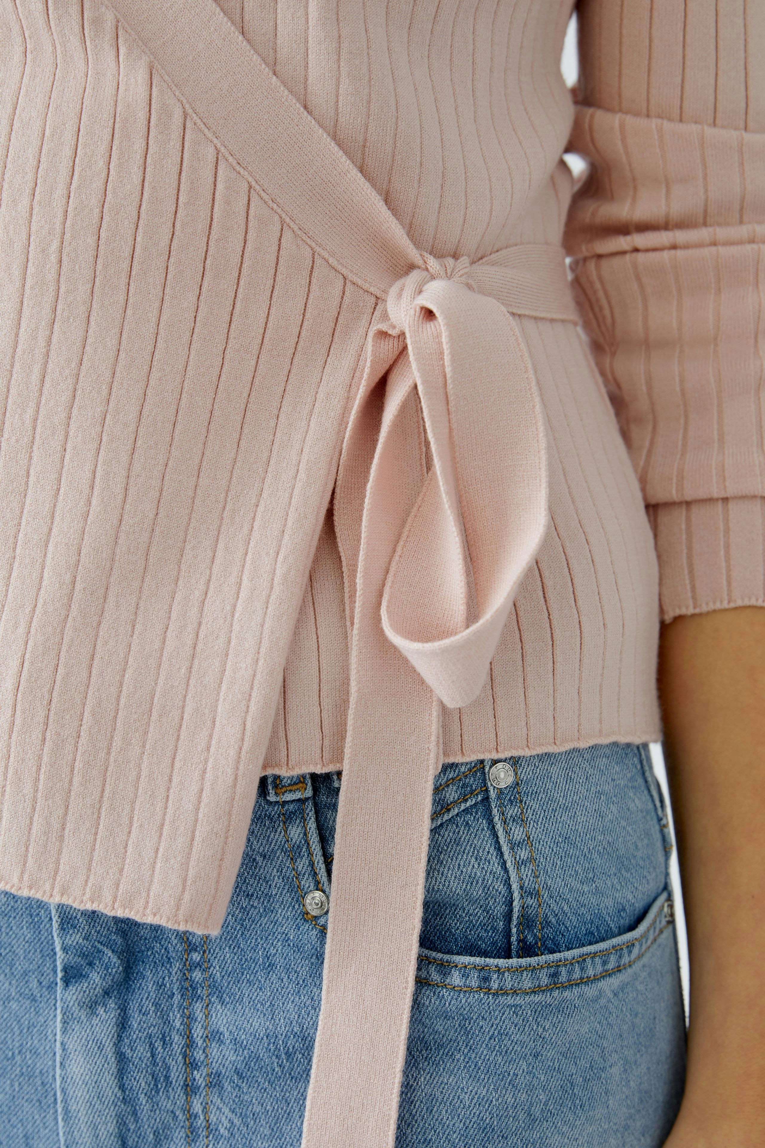 Stylish women's cardigan: A woman in a soft pink ribbed cardigan with a tied waist detail.