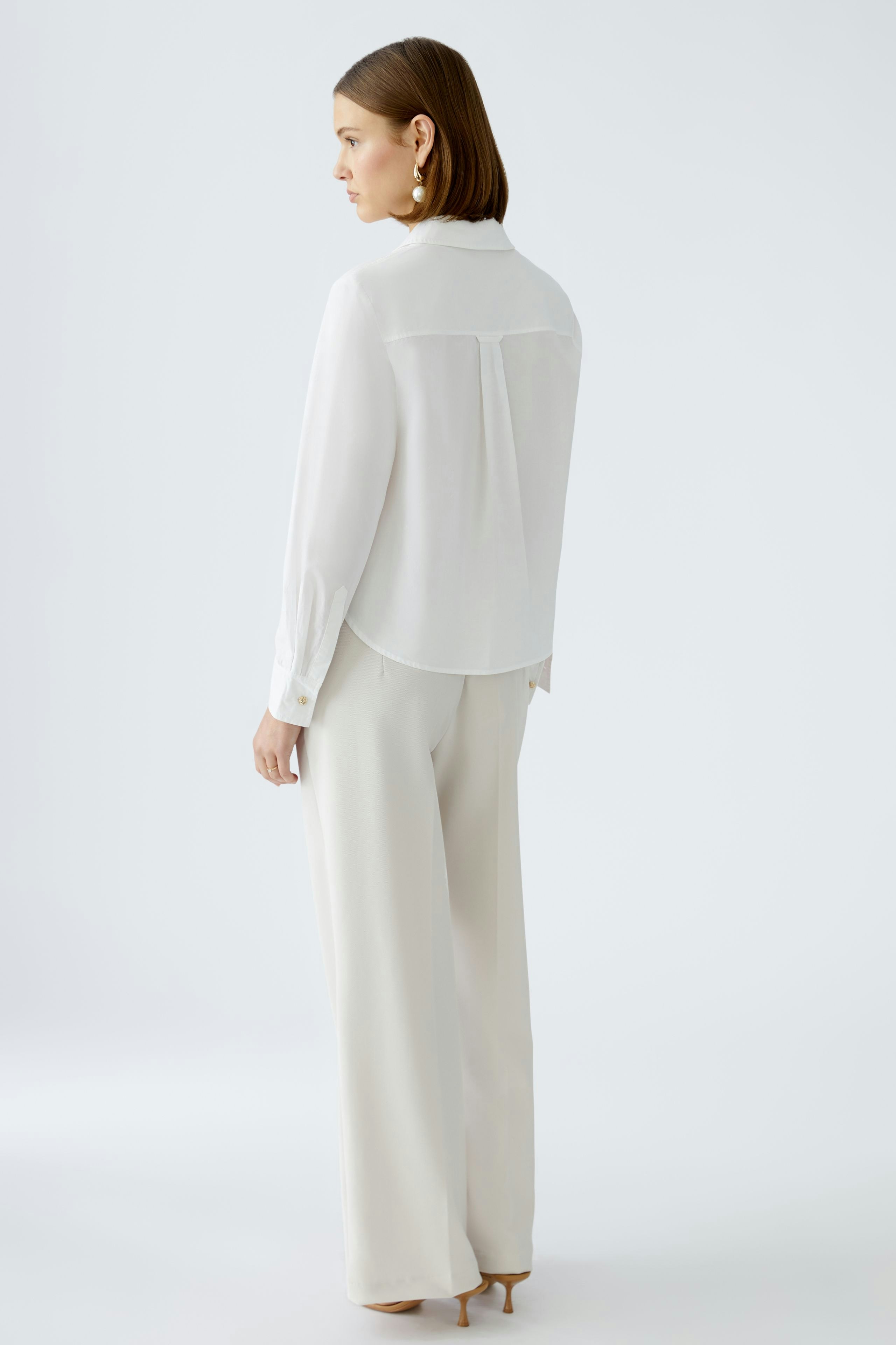 Elegante Damen-Bluse: Frau in weißer Bluse mit lässigem Schnitt und langen Ärmeln.