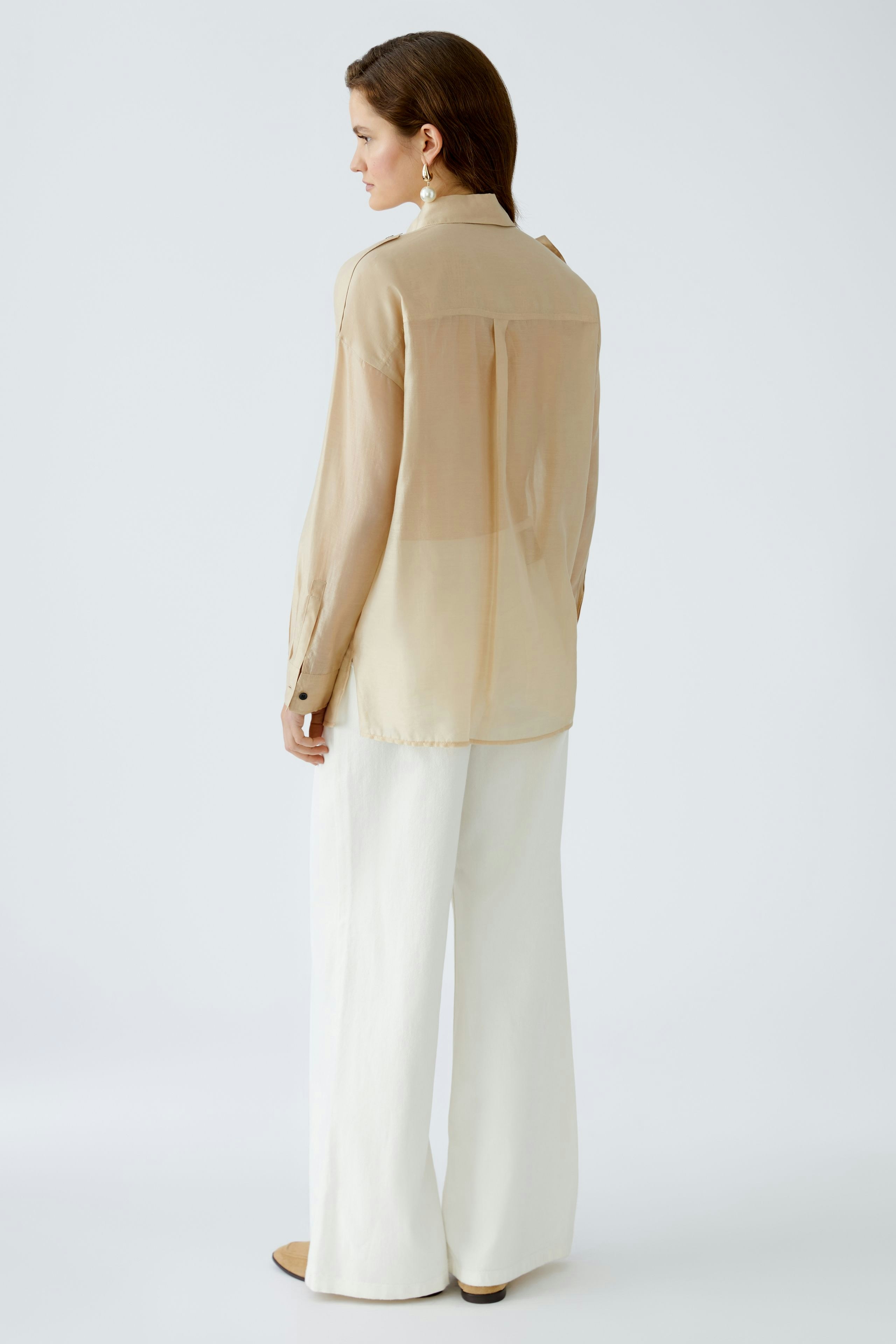 Elegant women's blouse: A woman in a light, sheer blouse paired with wide white trousers.