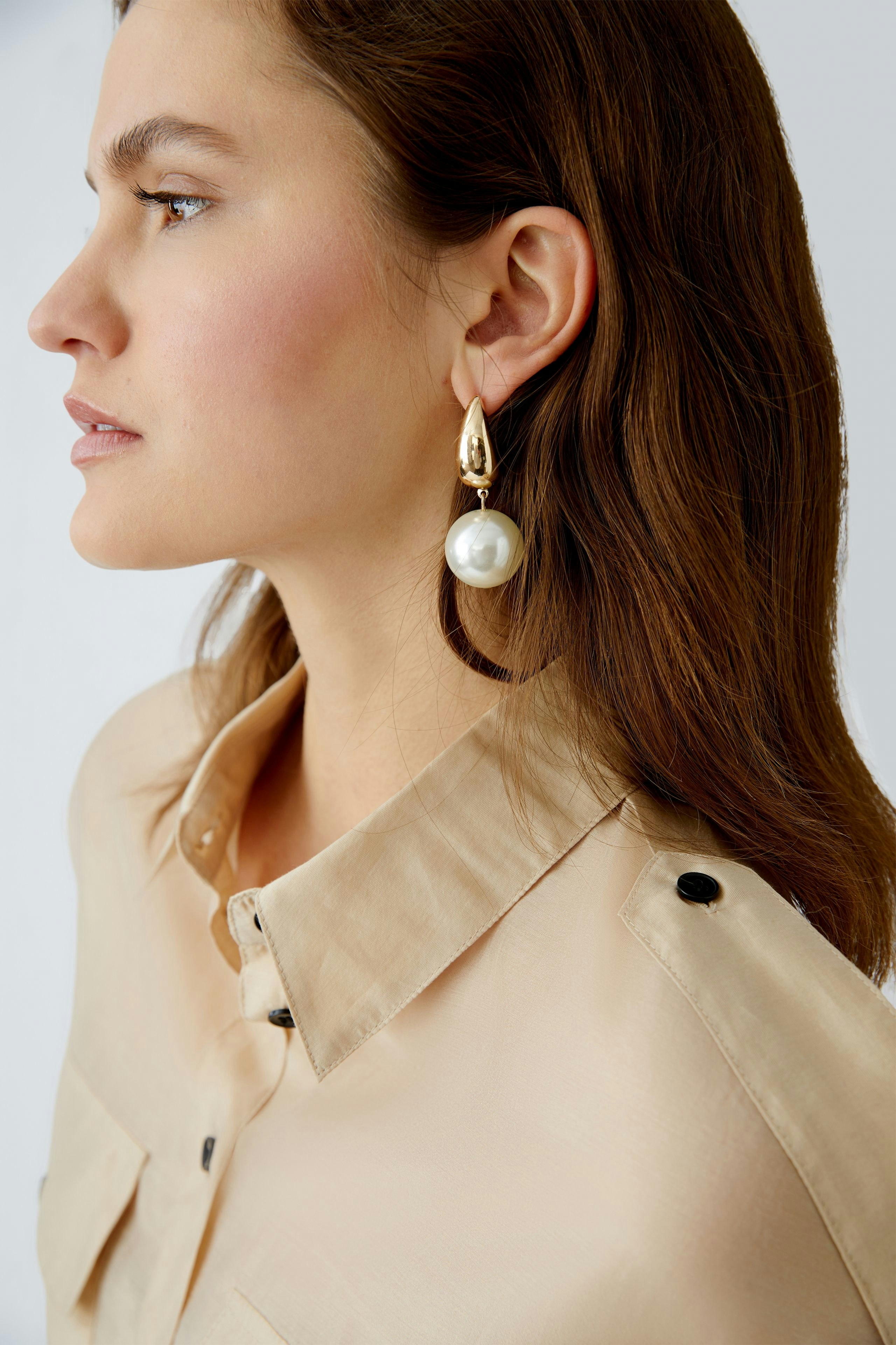 Elegant women's blouse: A woman in a light beige blouse with a classic collar and stylish earrings.