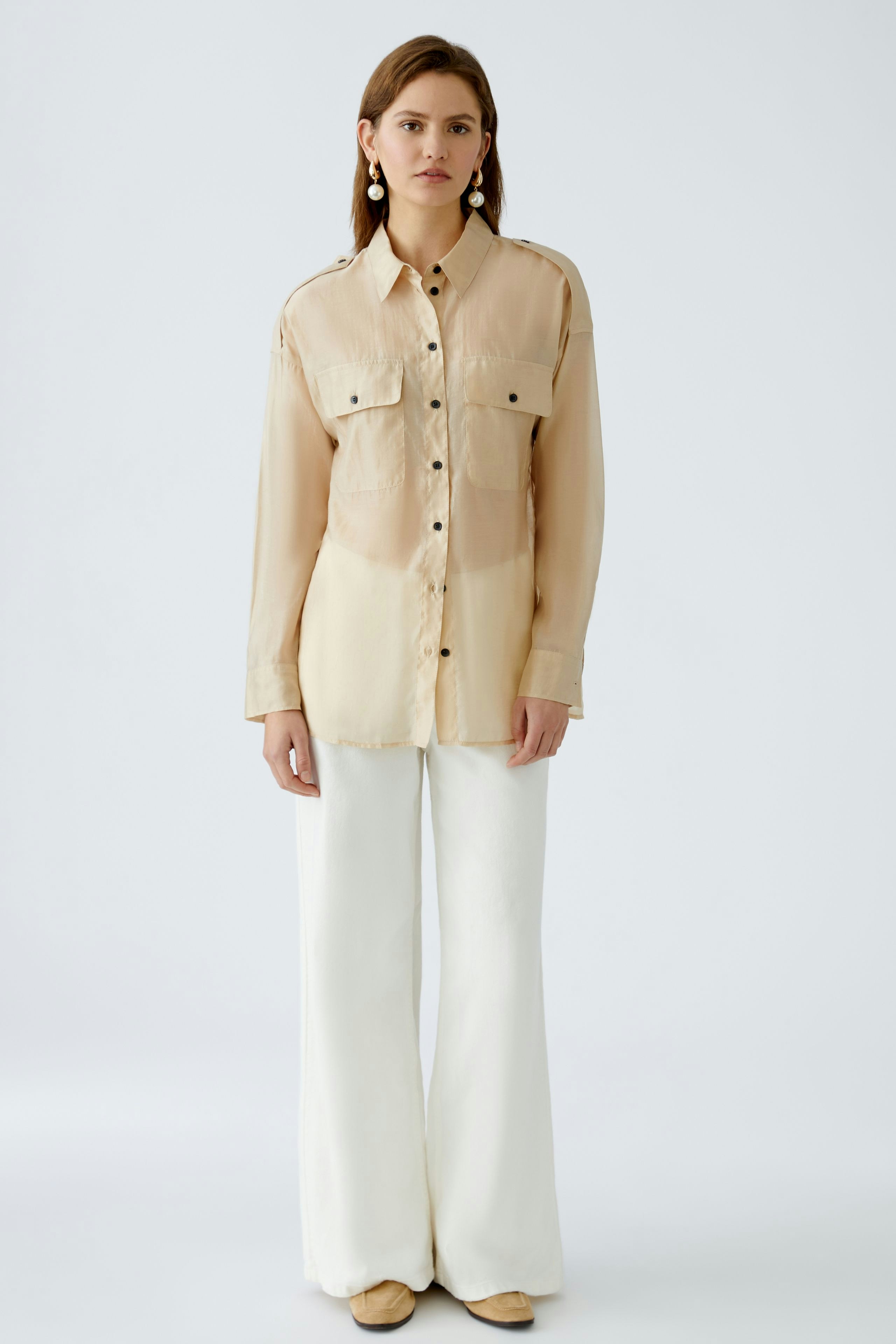 Chic women's blouse: A woman in a light beige blouse with pockets, paired with white wide-leg pants.