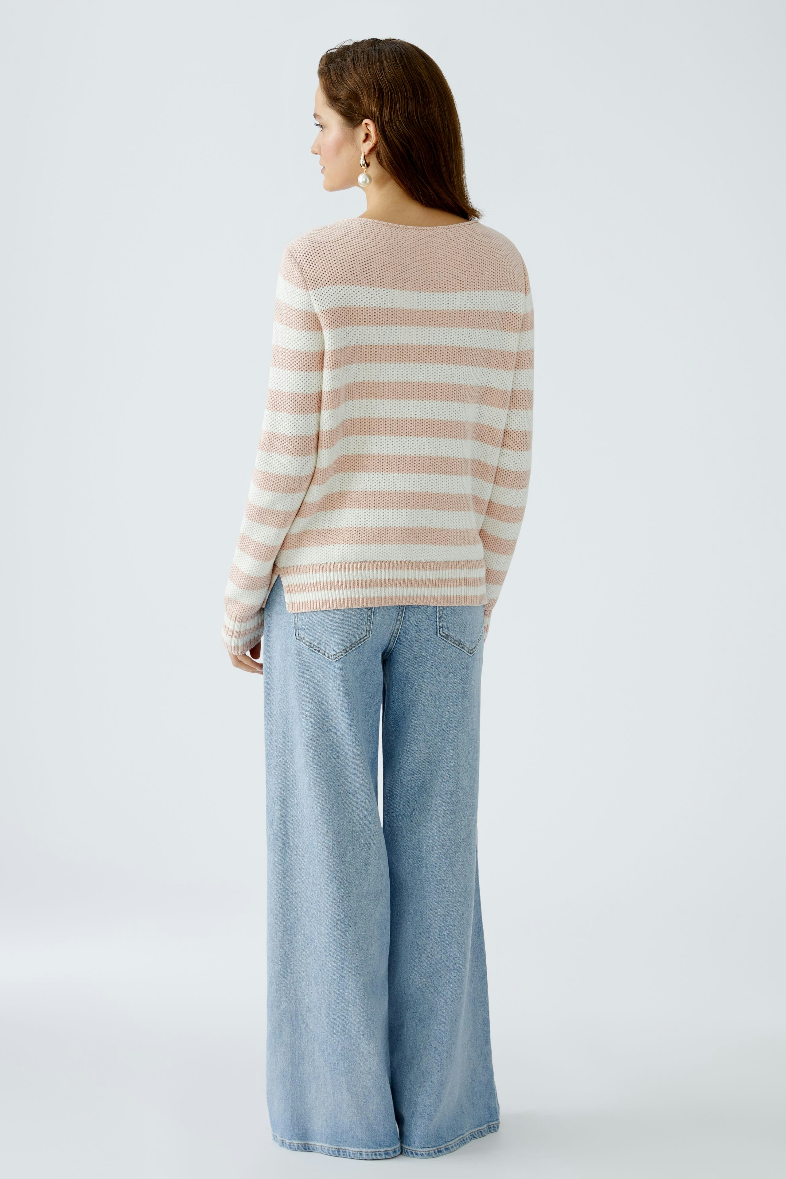 Damen-Pullover: Frau trägt einen gestreiften Pullover in sanften Farben, kombiniert mit weiten Jeans.