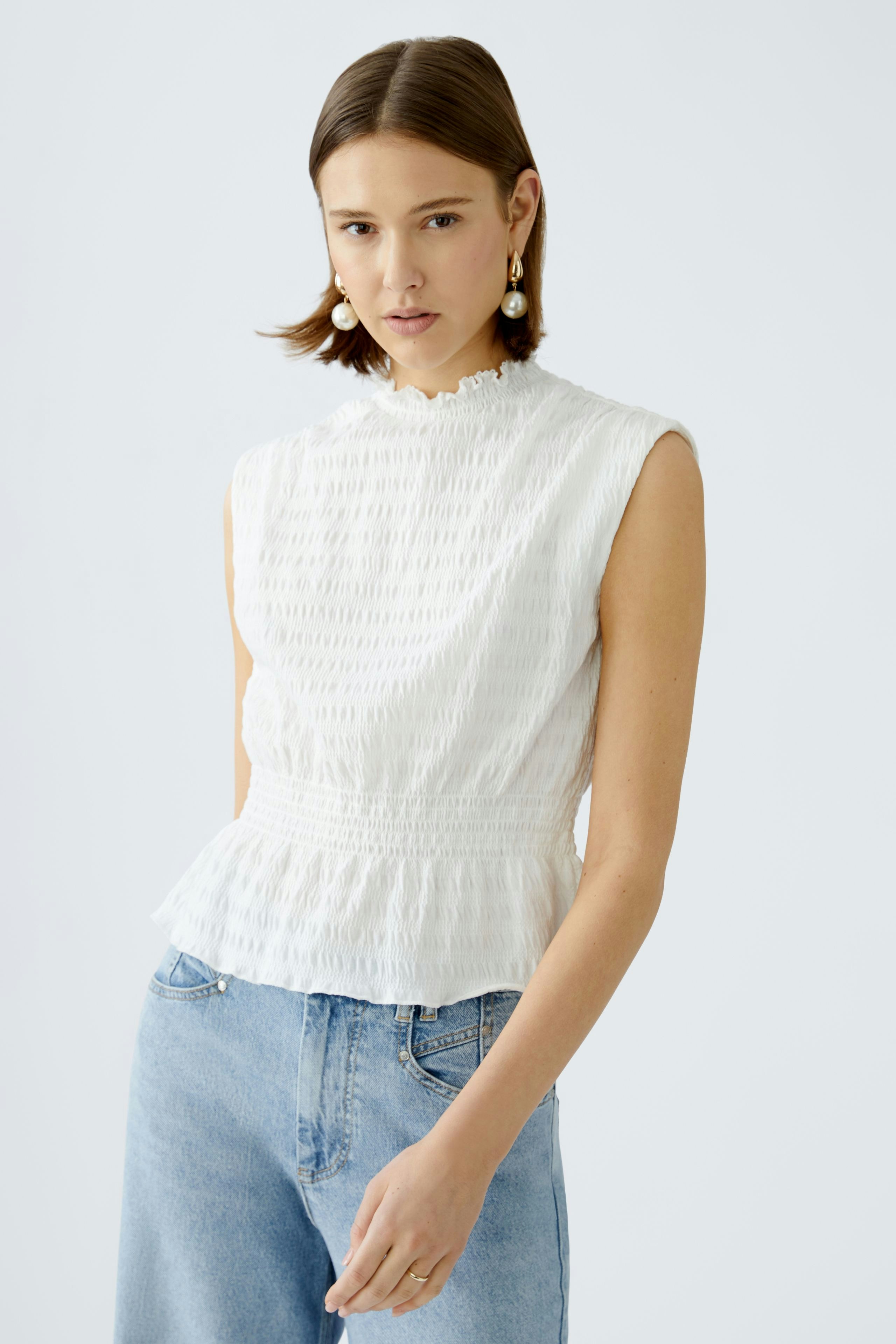 Elegant women's top: A woman in a white textured top with a peplum hem, styled with casual jeans.