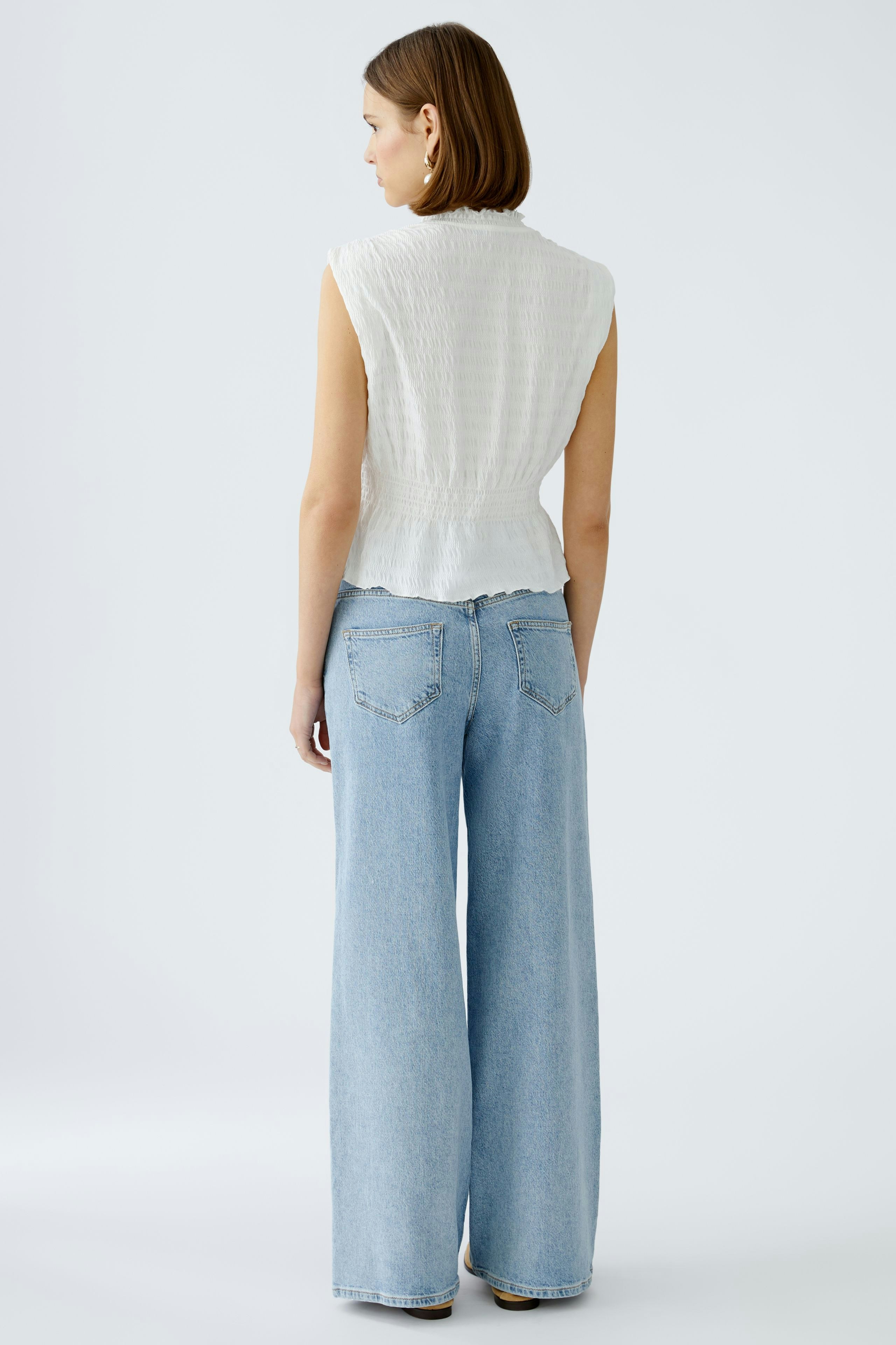 Stylish women's top: A woman in a white sleeveless top paired with wide-leg jeans.