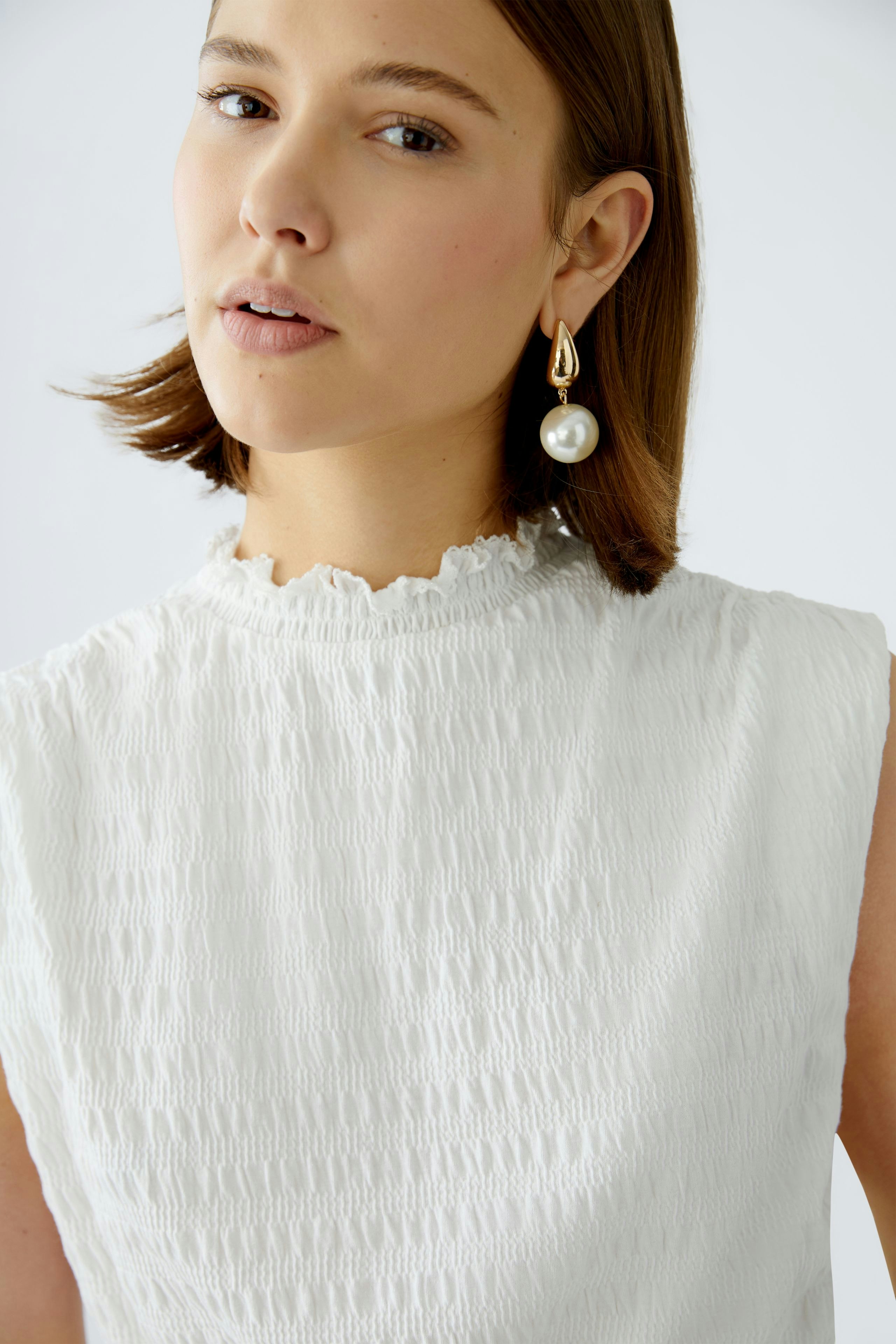 Elegant women's top: A woman in a textured white sleeveless top with a ruffled neckline.