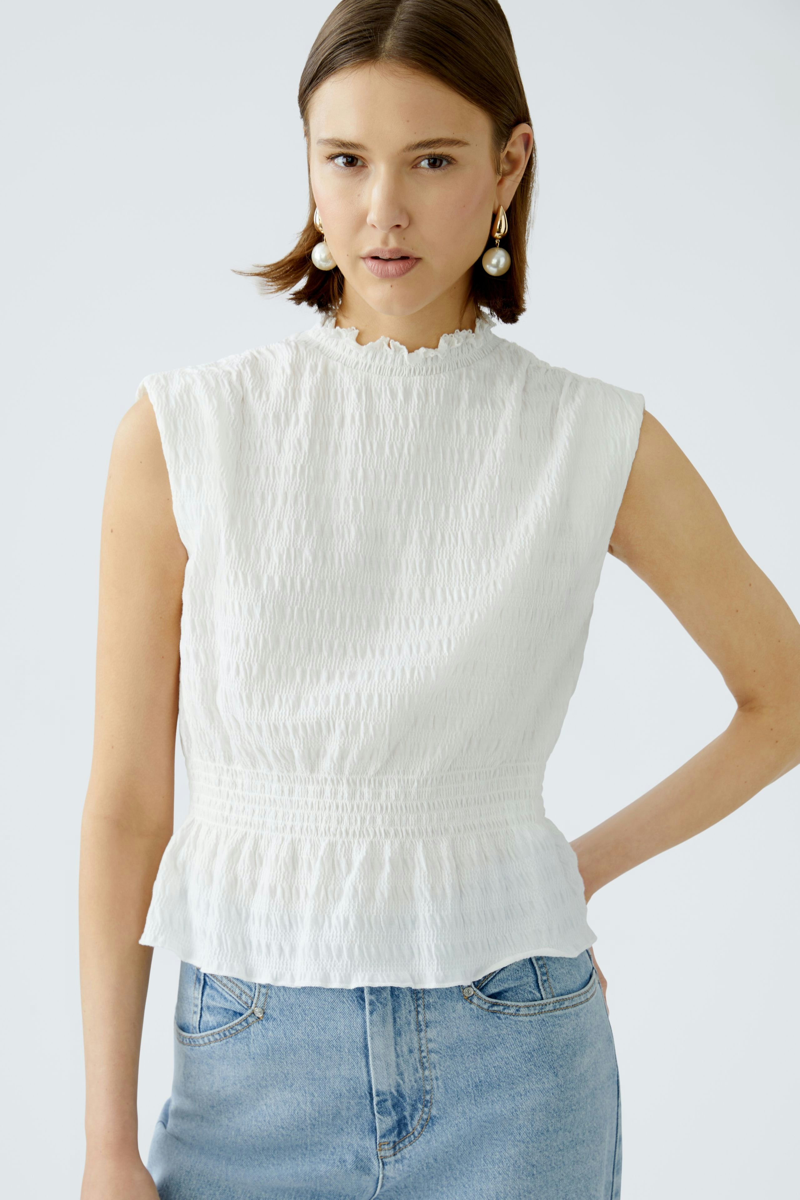 Elegant women's top: A woman in a white textured top with a peplum waist, styled with denim.