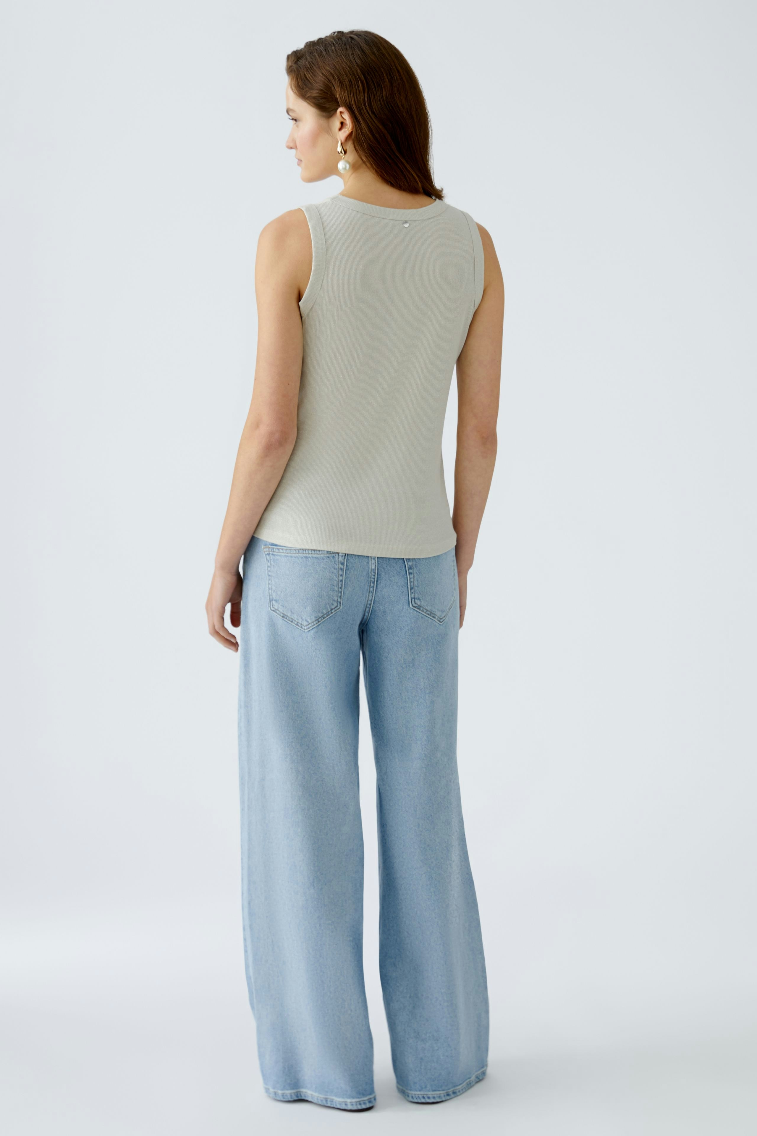 Stylish women's top: A woman in a light gray sleeveless top paired with wide-leg jeans.