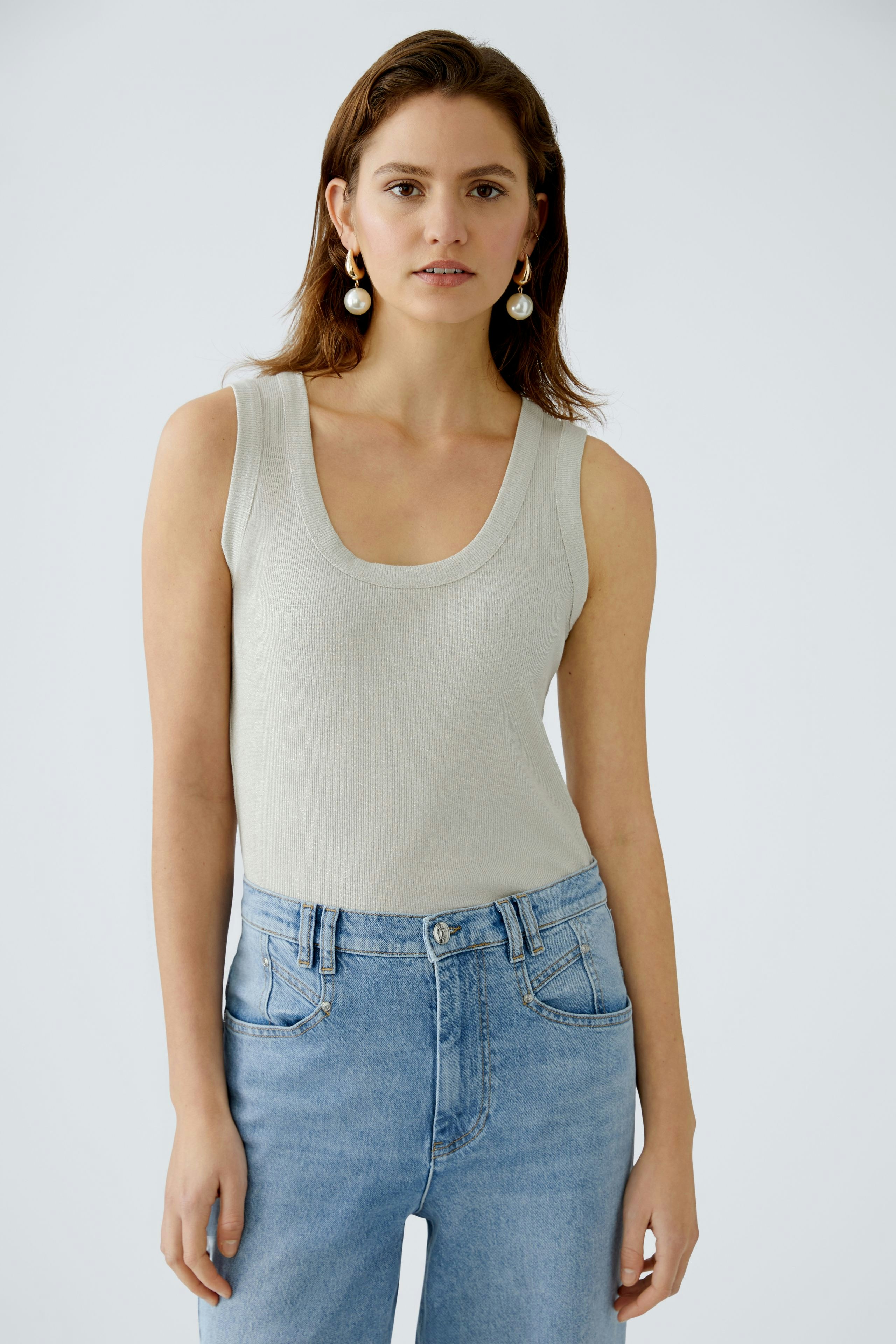 Stylish women's top: A woman in a light grey sleeveless top paired with high-waisted jeans.