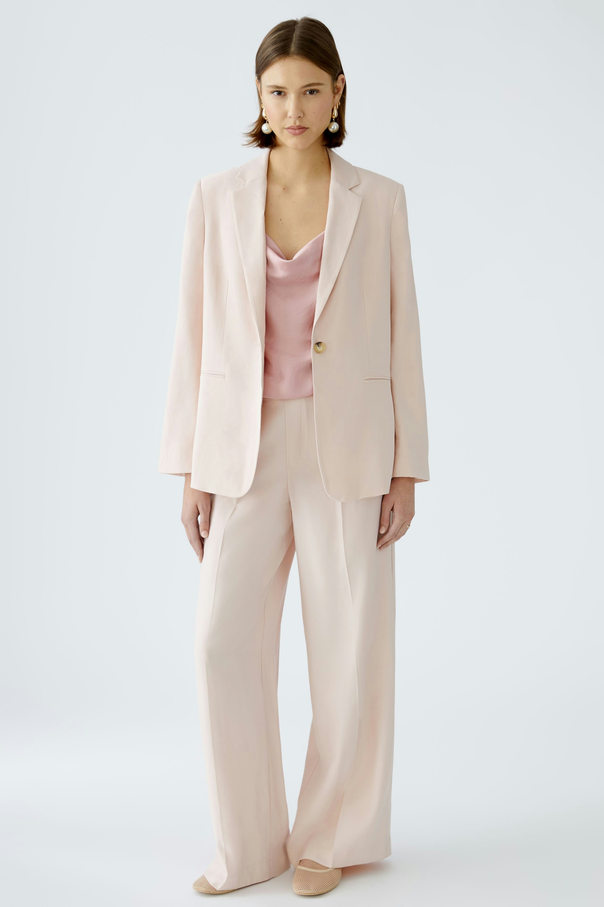 Elegant women's pleated trousers in soft pink, paired with a matching top and blazer.