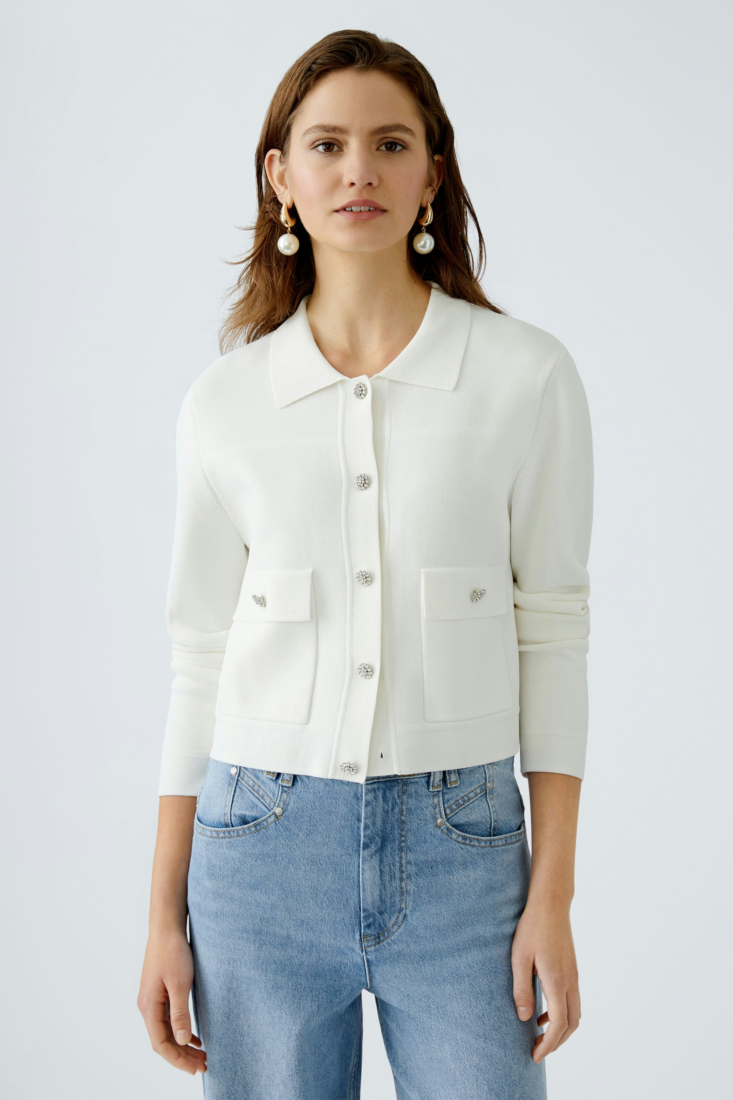 Chic women's cardigan: A woman in a white cardigan with pockets, paired with blue jeans, exuding elegance.