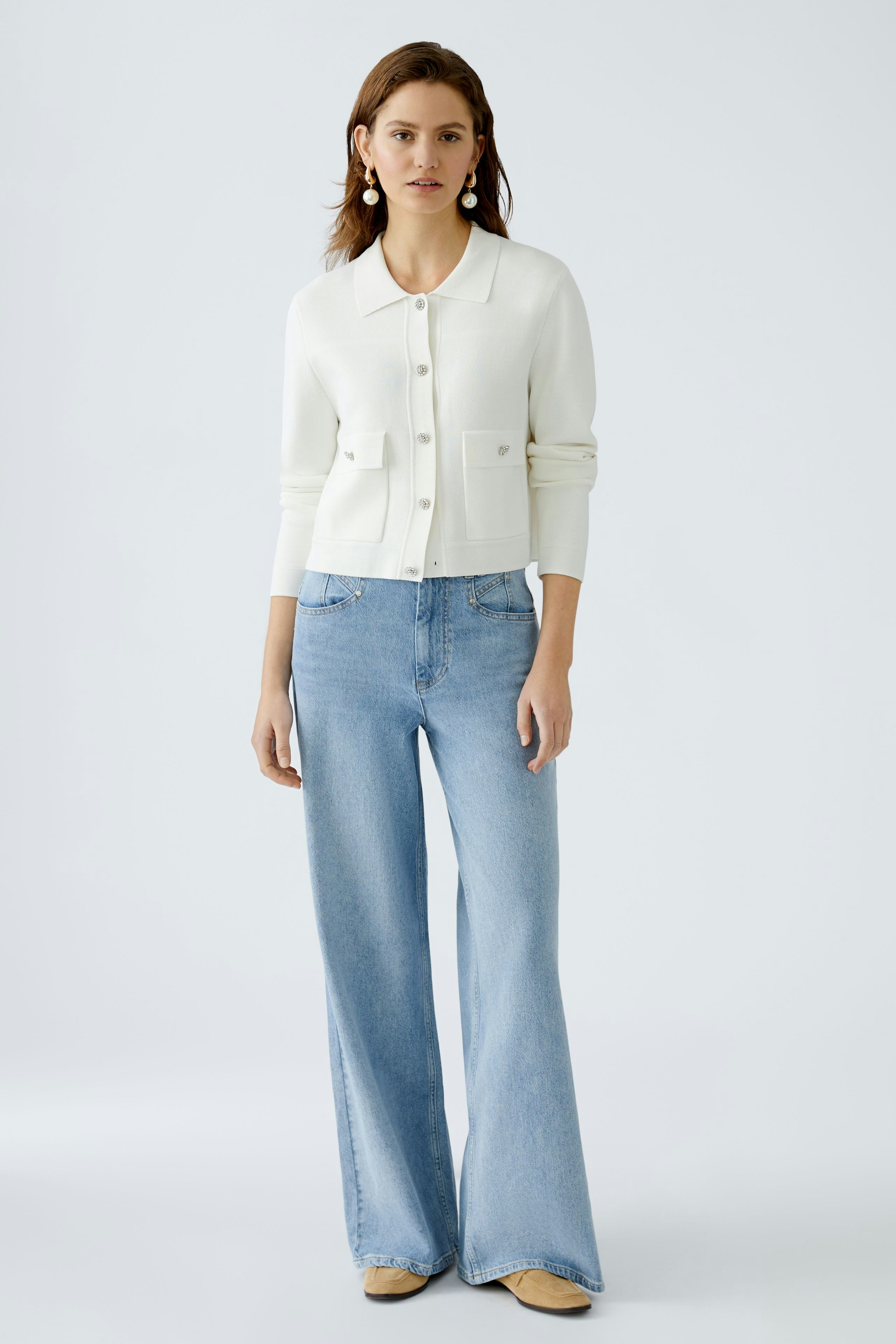 Chic women's cardigan: A woman in a white cardigan with pockets, paired with light blue wide-leg jeans.